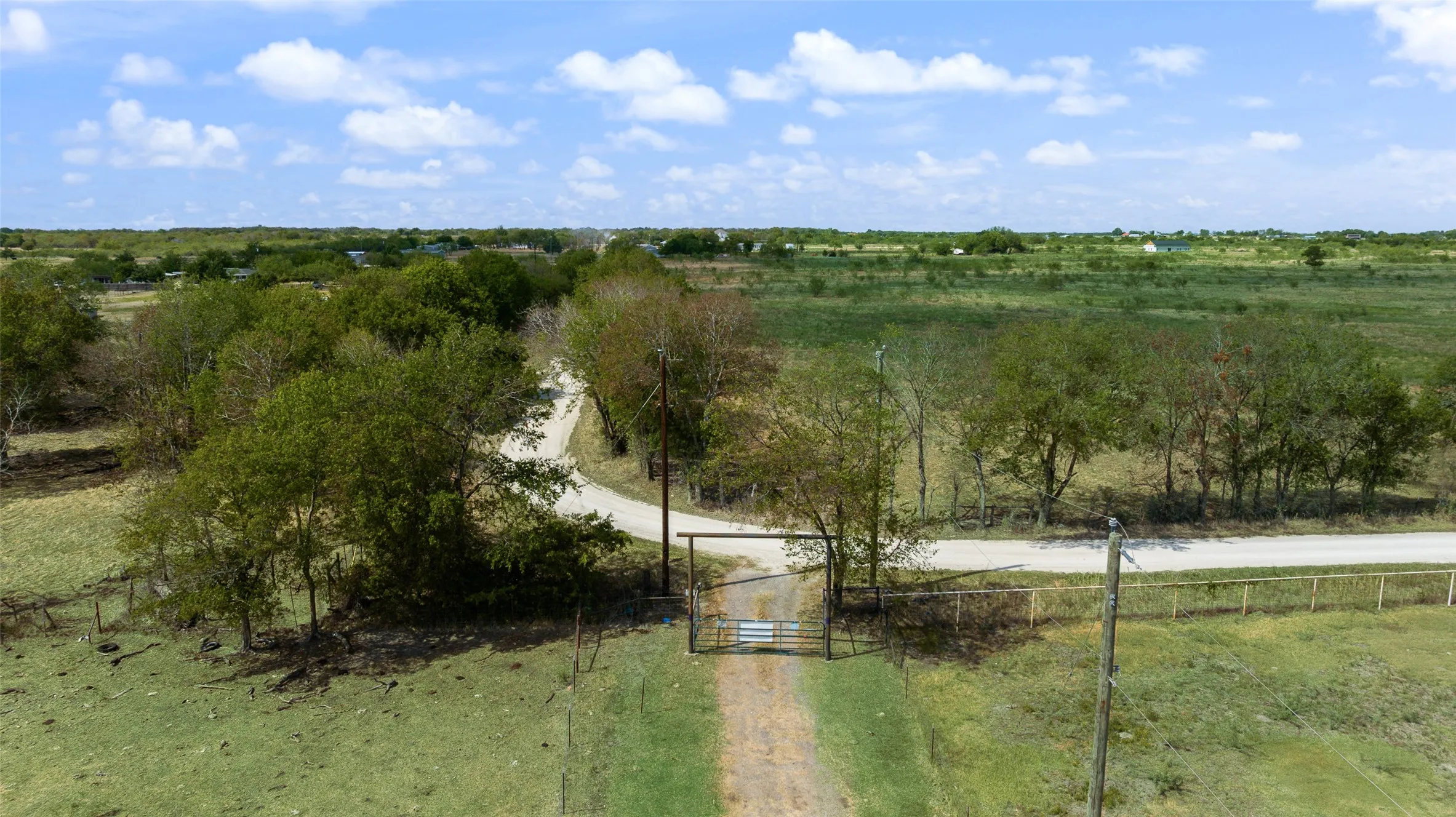 Gated entry with a gravel drive, expansive open fields, and mature trees