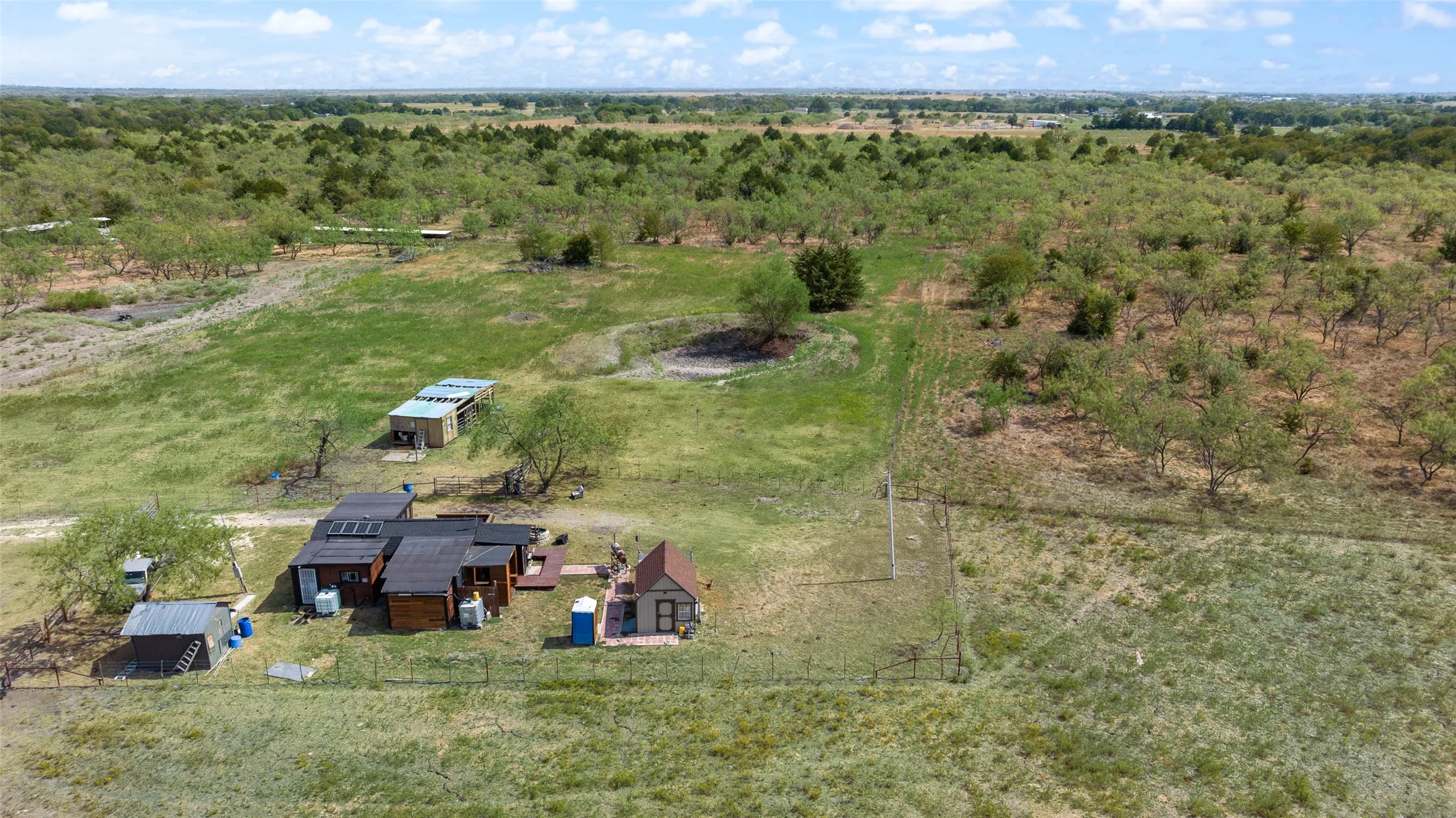 Expansive rural property featuring a main structure, outbuildings, and a fenced perimeter