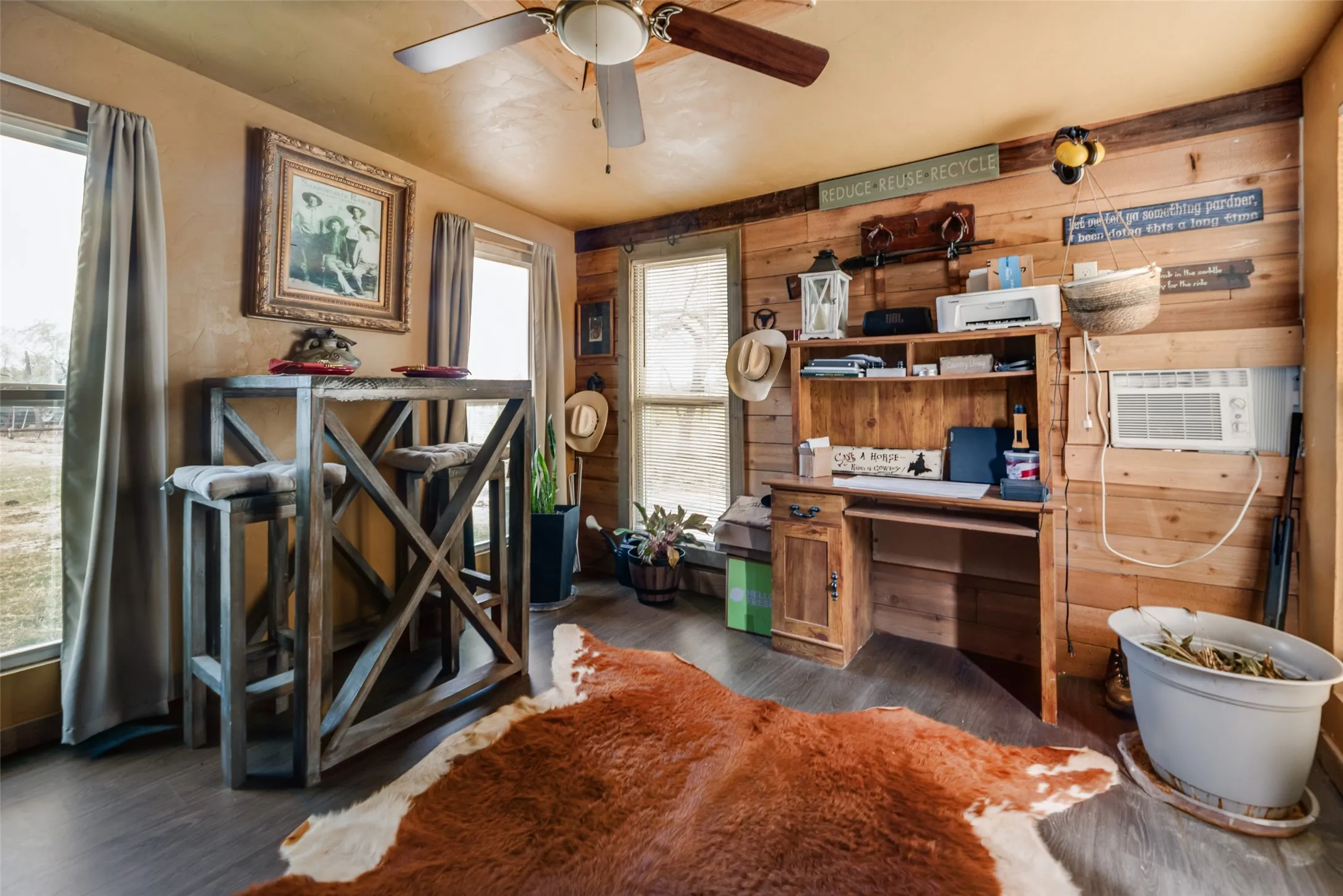 Built-in desk area, wood-finish flooring, wood plank accent wall, ceiling fan, and multiple windows providing natural light