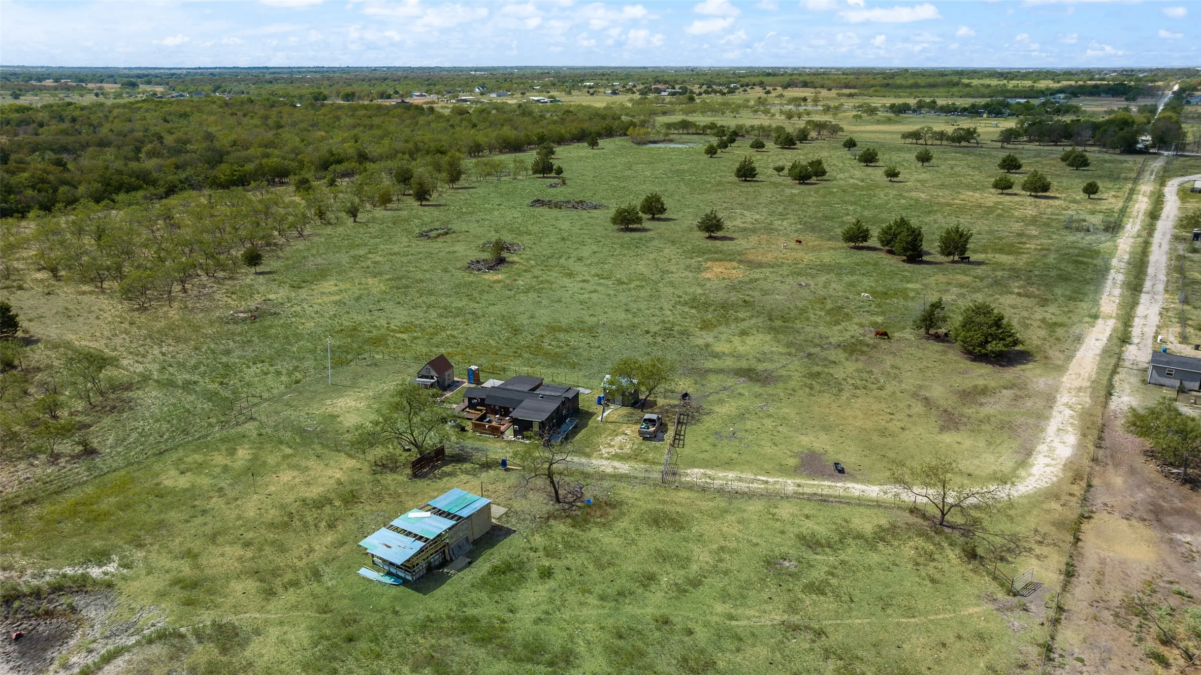 Expansive open land featuring a residence, detached structure, and scattered trees