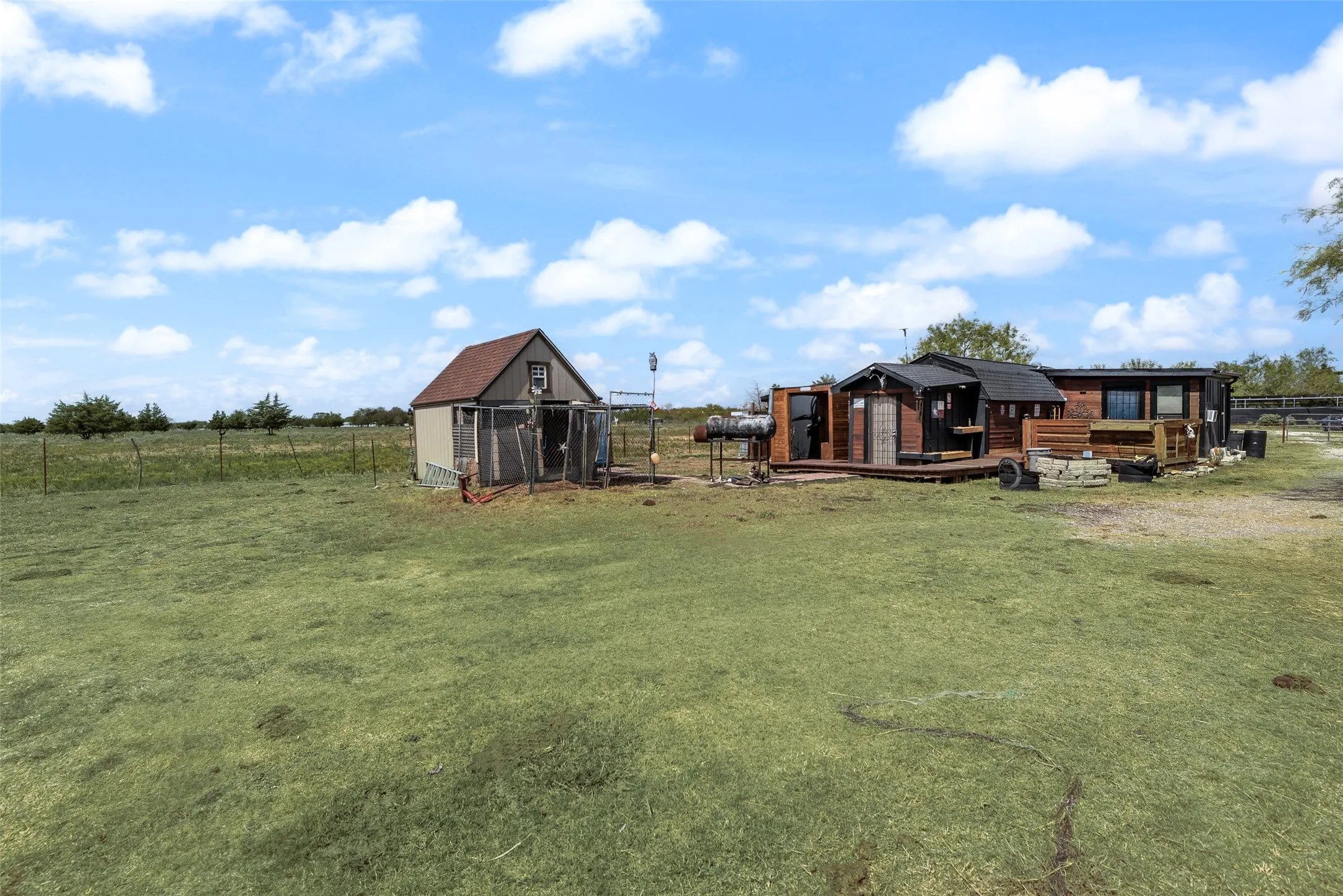 Expansive outdoor area with a wood-sided structure, a separate storage shed, and a large grassy field