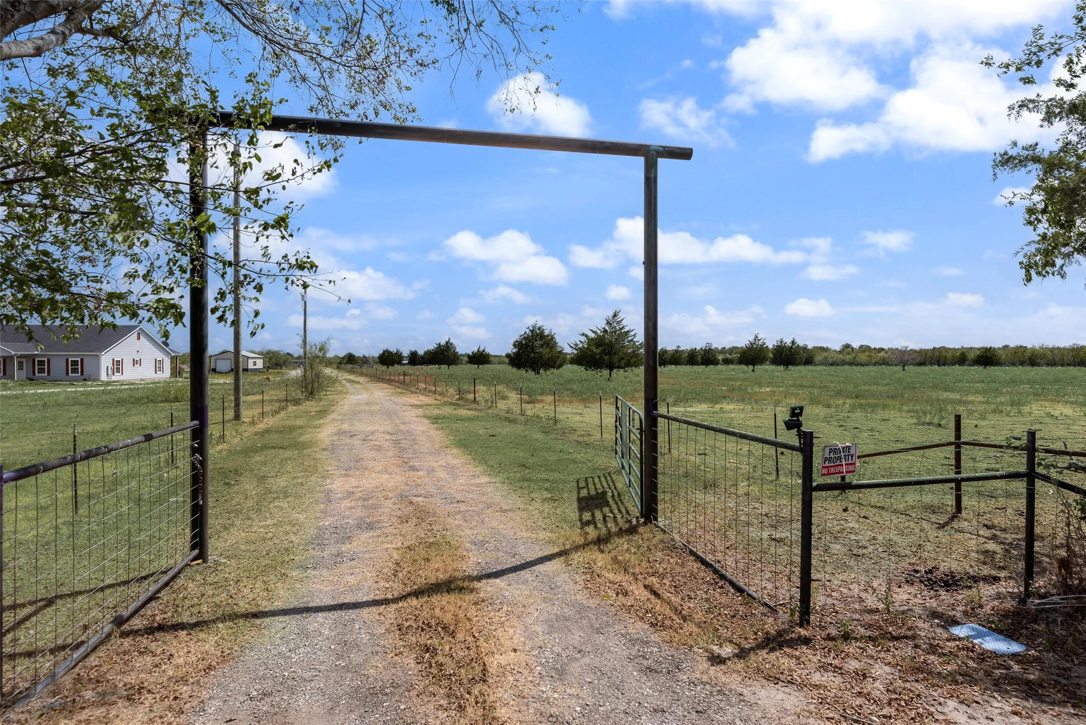 Gated entry with a gravel drive, expansive open fields, and a distant single-story structure