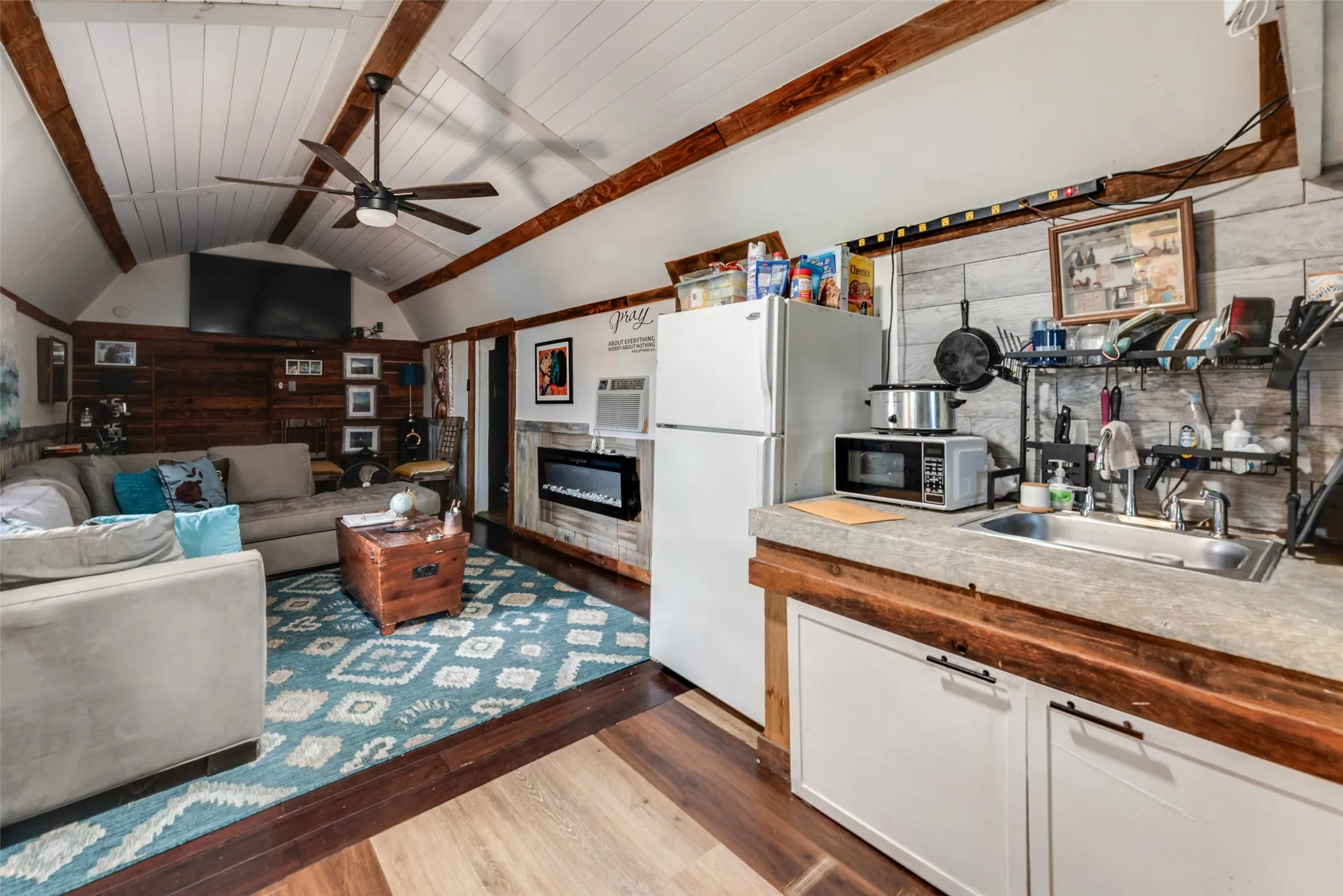 Vaulted plank ceiling with exposed wood beams, wood-finish flooring, and a ceiling fan