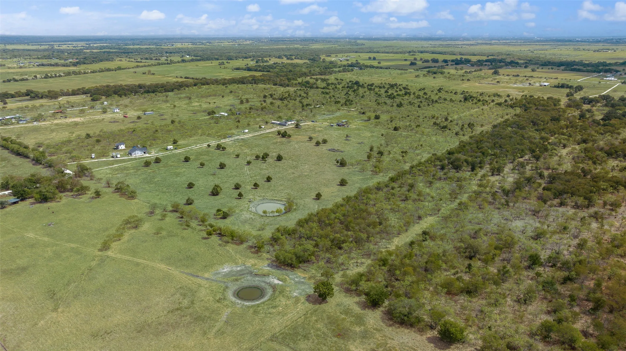 Expansive property featuring varied terrain, multiple established trees, and two visible ponds