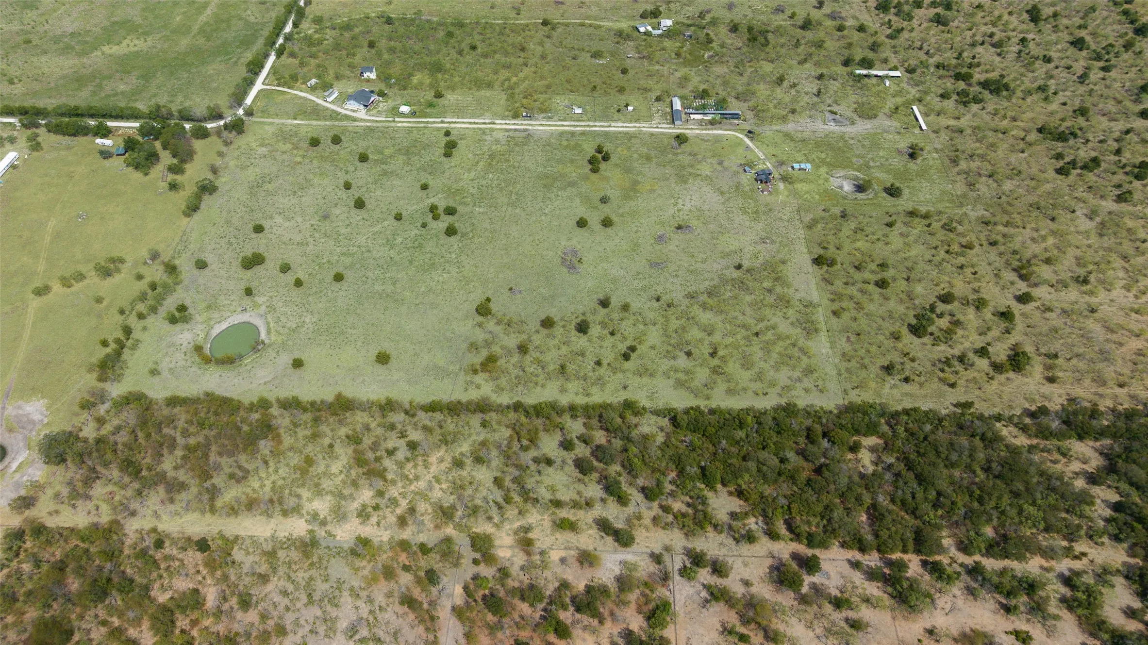 Expansive open land featuring diverse vegetation, a natural pond, and a defined treeline