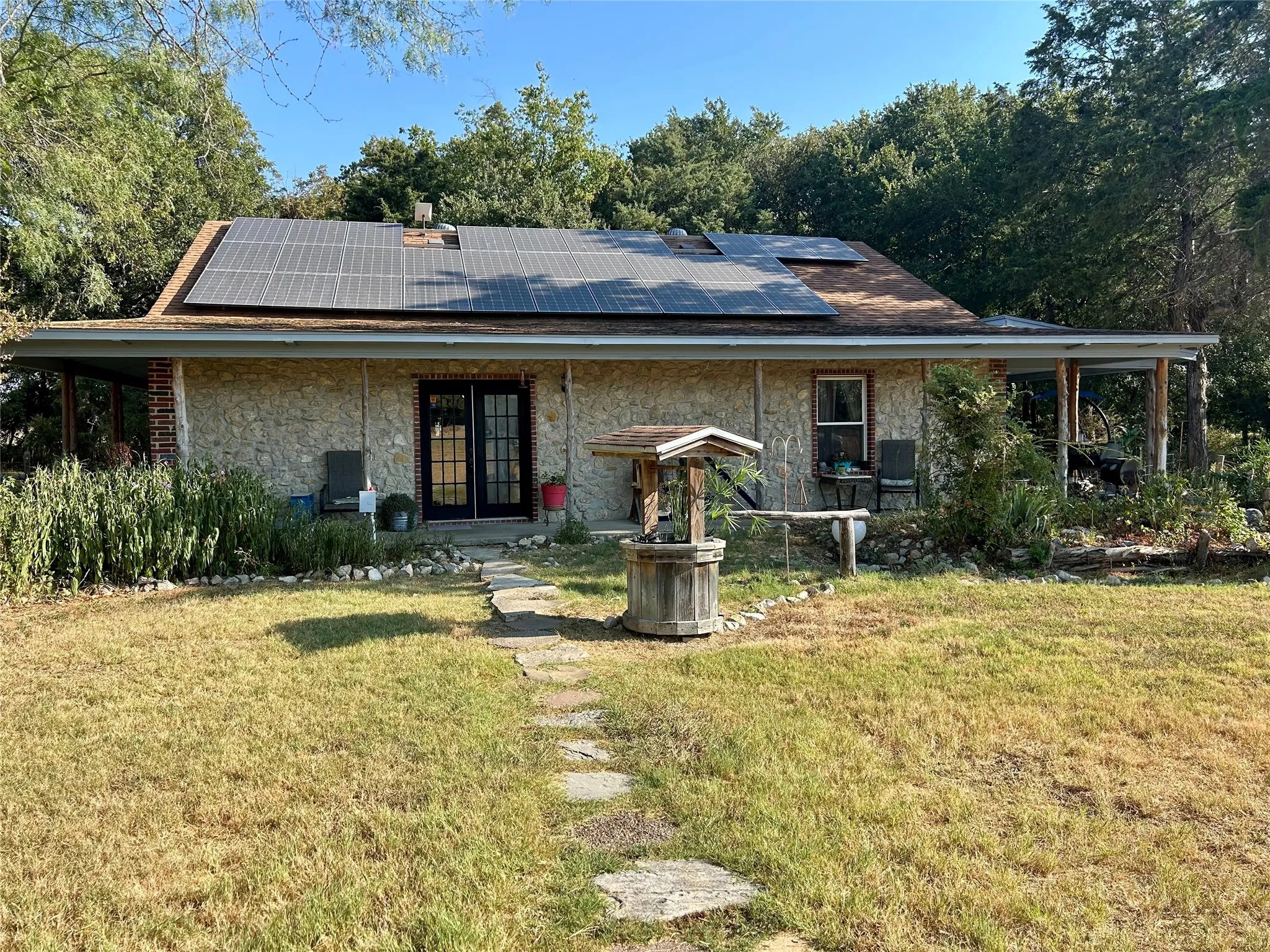 Stone facade residence with solar panels, covered porch, and double French doors