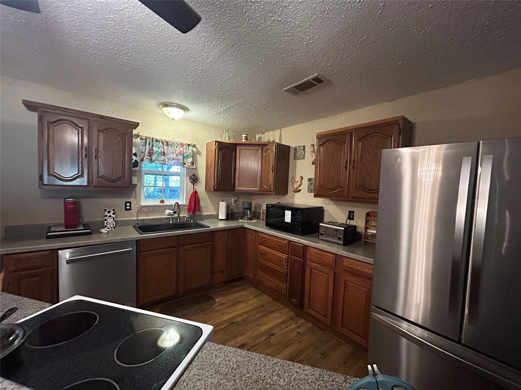 Kitchen featuring wood cabinetry, stainless steel appliances, a black sink, and wood-finish flooring