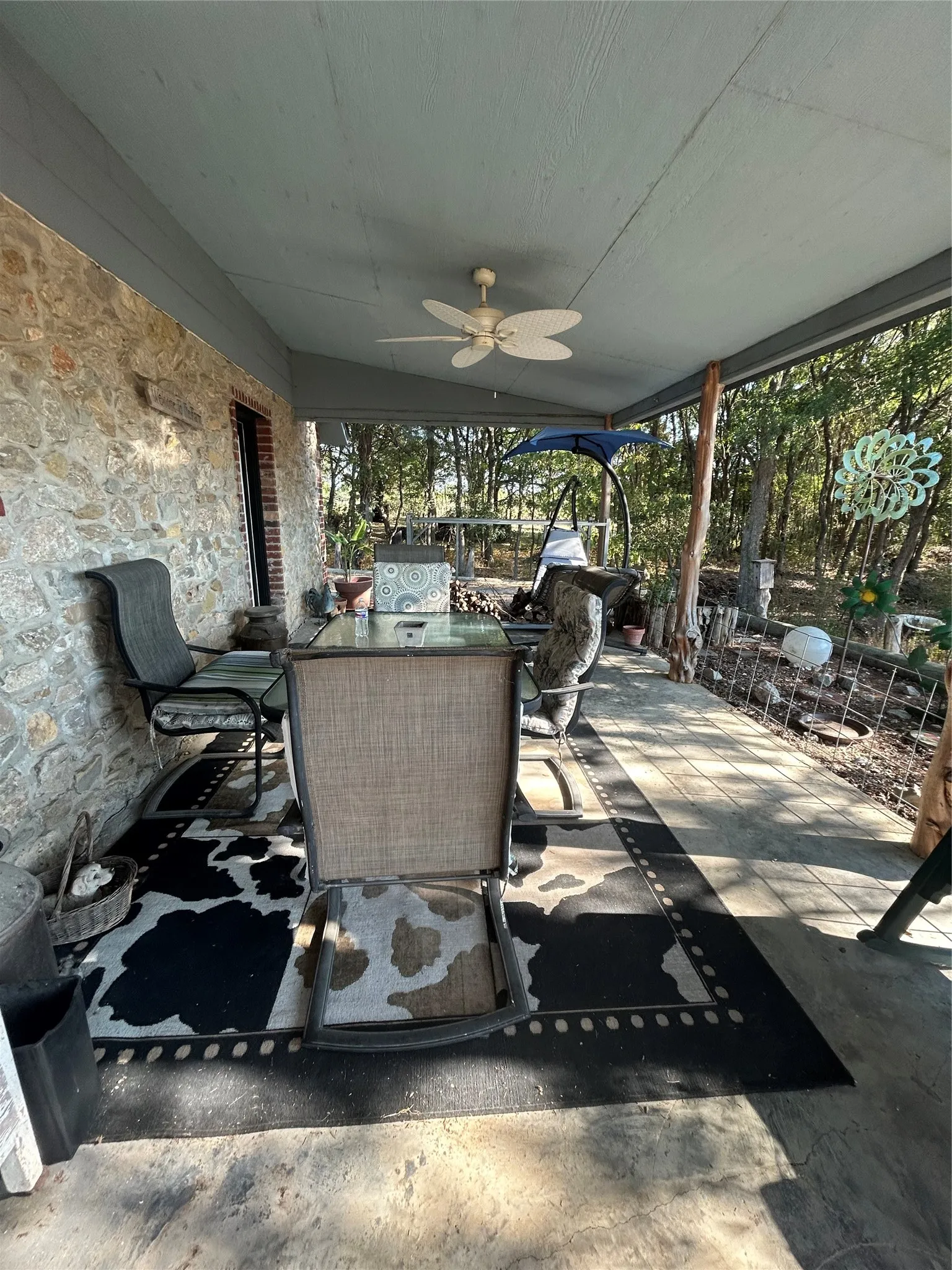 Covered patio featuring a stone exterior wall, ceiling fan, and concrete flooring