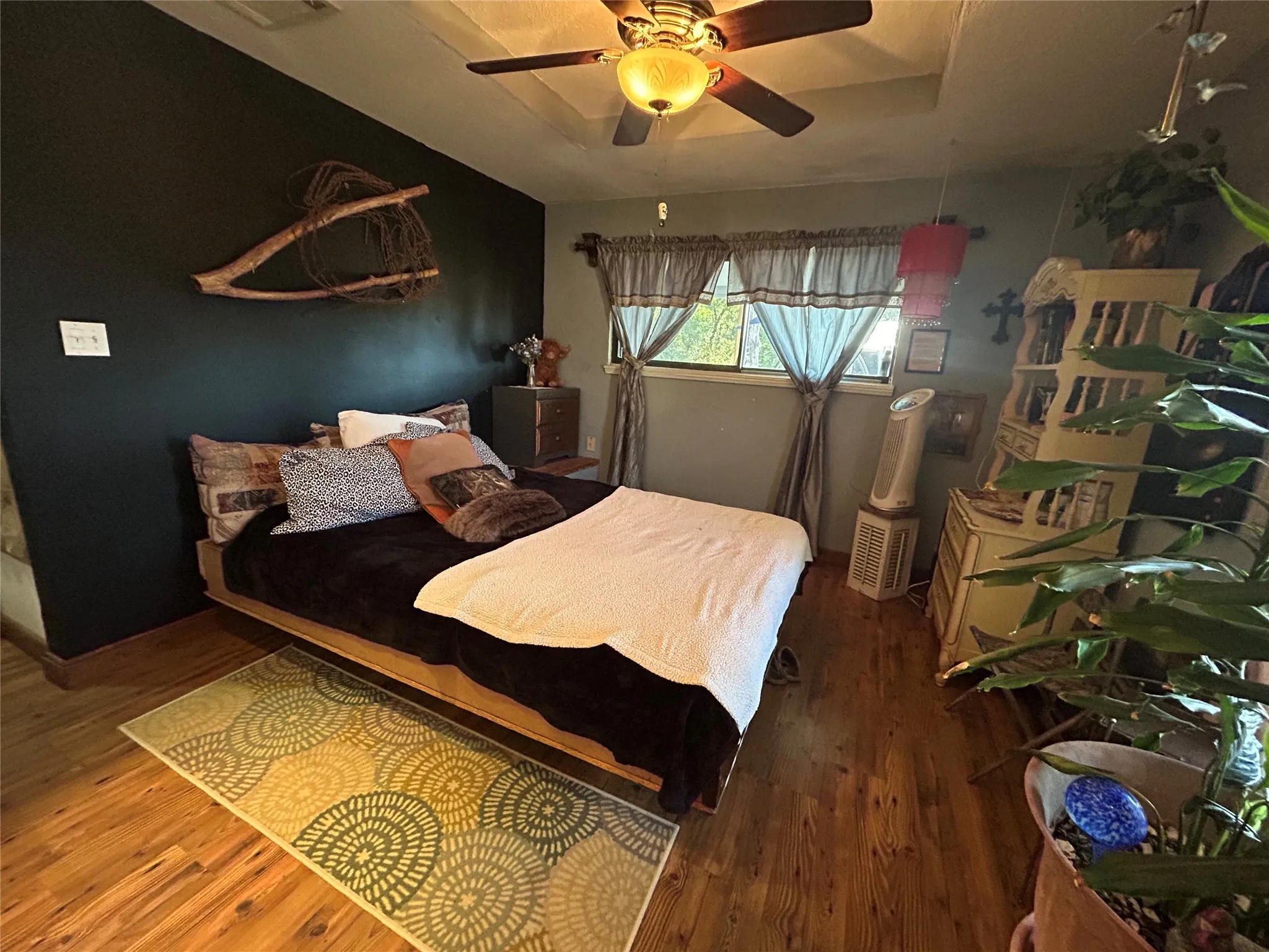 Wood-finish flooring, ceiling fan with integrated lighting, and multiple windows with curtain rods