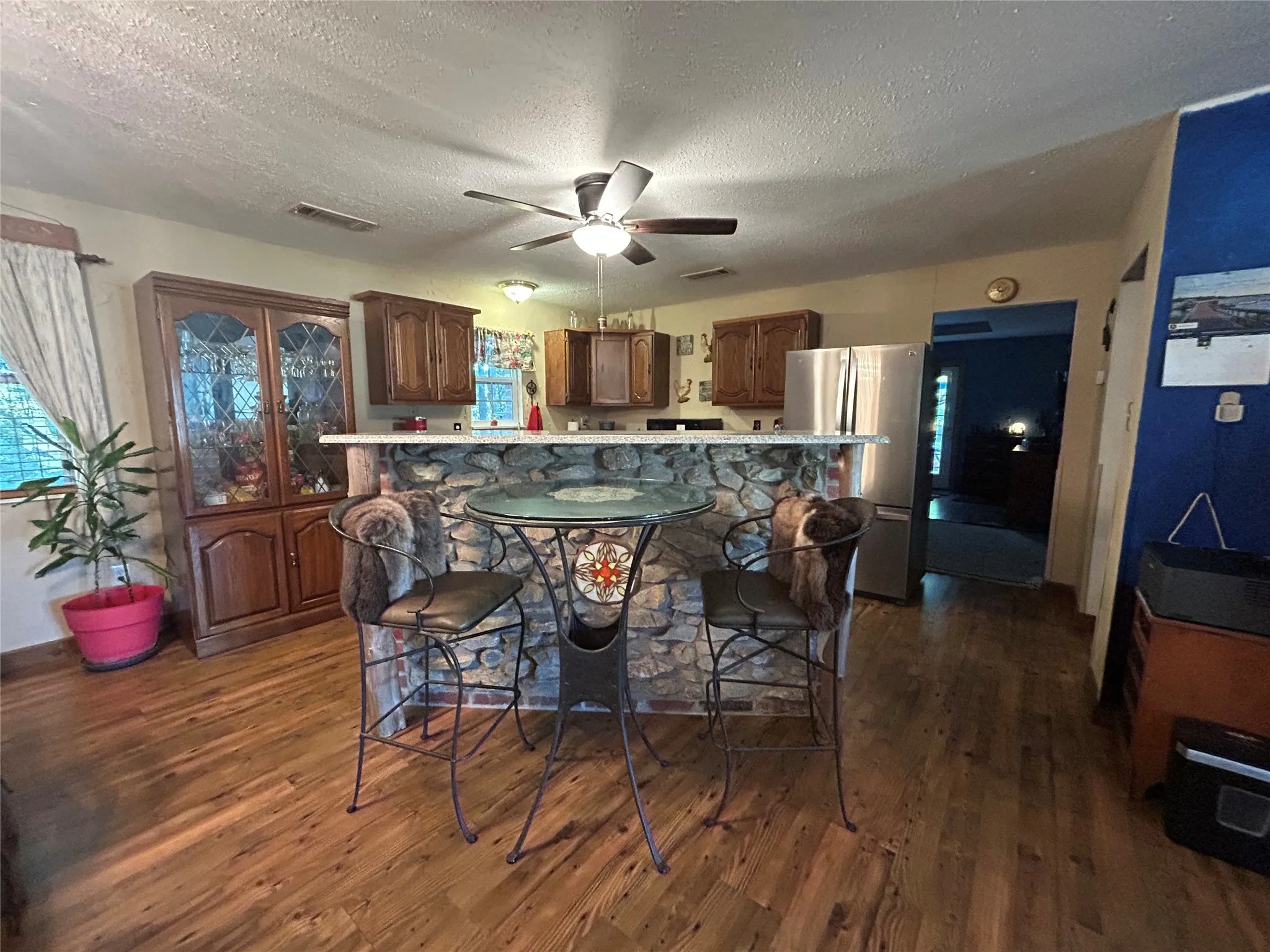 Wood-finish flooring throughout, stone-clad breakfast bar, wood cabinetry, stainless steel refrigerator, and ceiling fan