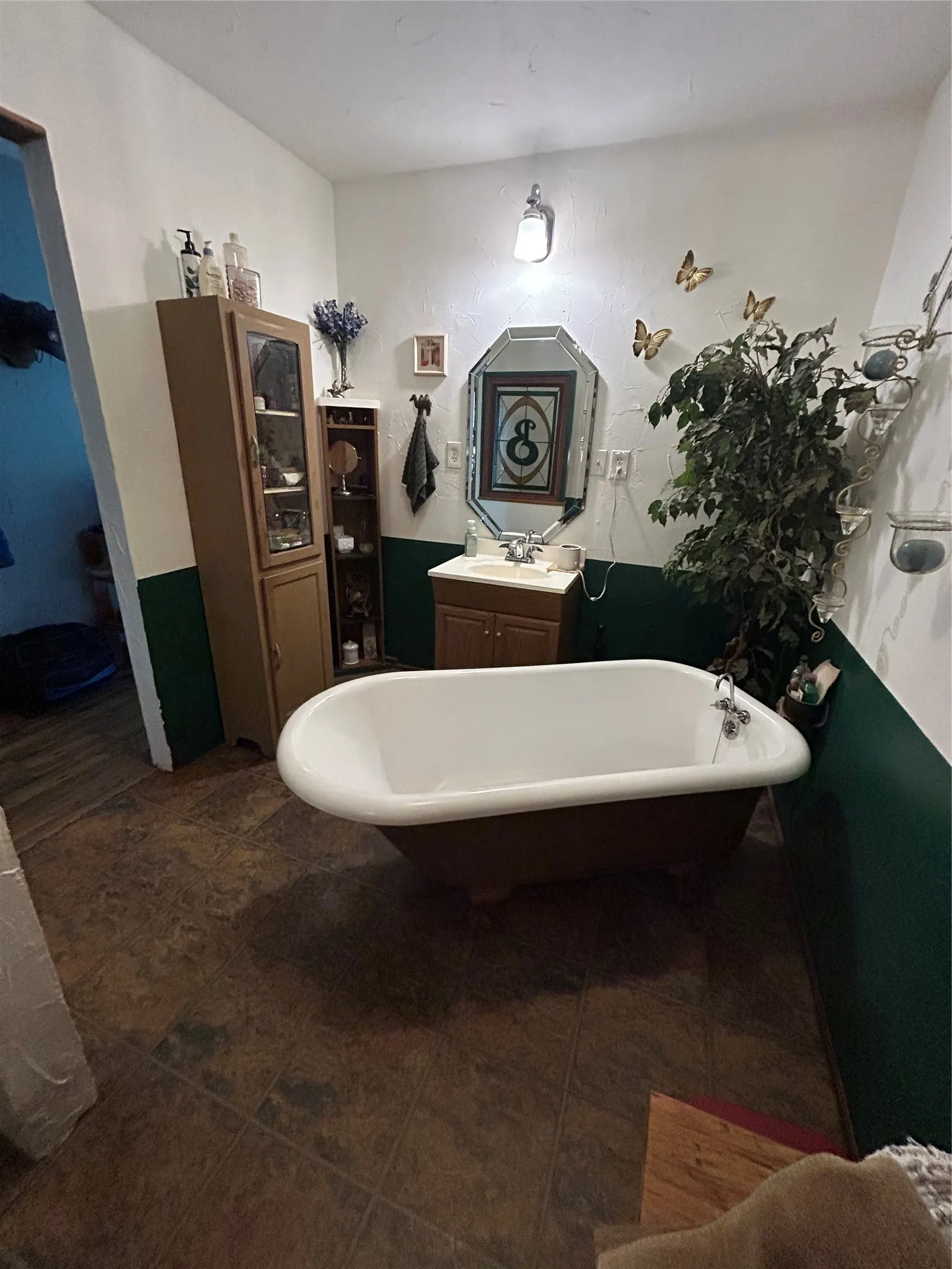 Free-standing bathtub, single vanity with integrated sink, wall-mounted light fixture, and wood-finish flooring