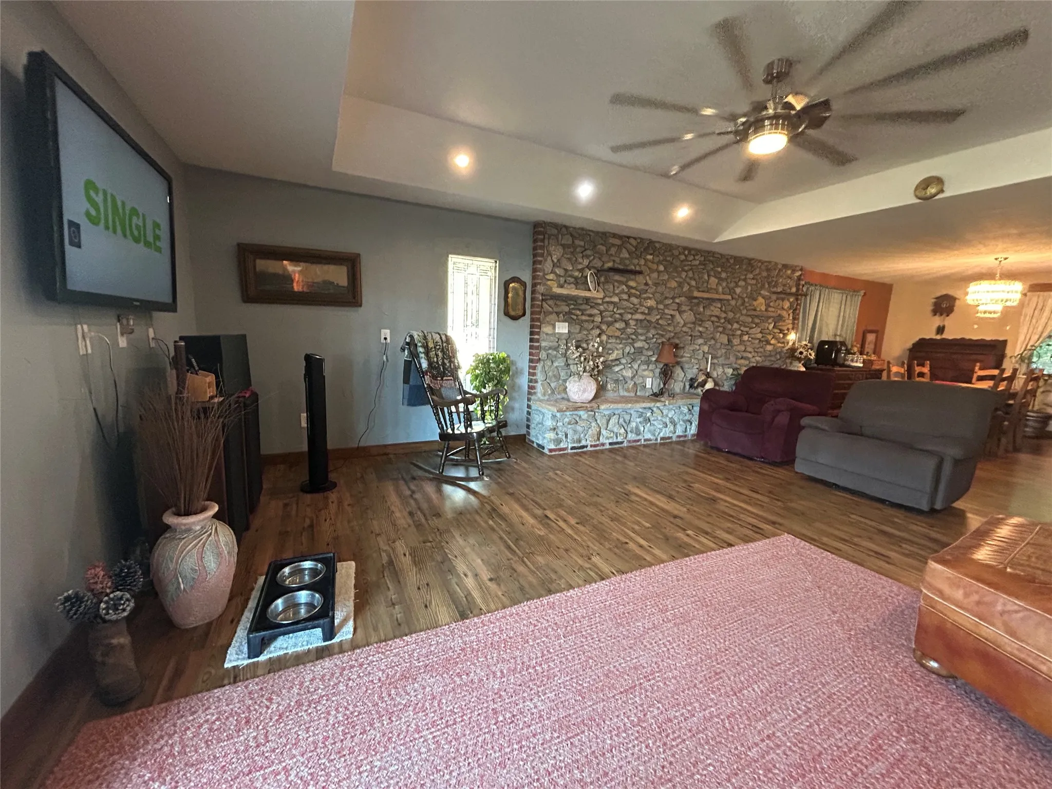 Stone-faced fireplace with a brick hearth, wood-finish flooring, recessed lighting, and a multi-blade ceiling fan