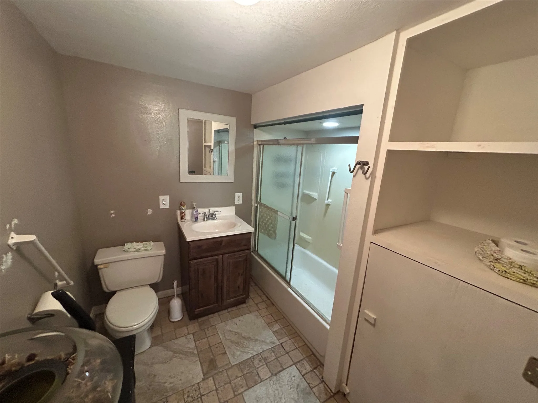 Bathroom featuring a vanity with a white basin and dark wood-finish cabinetry, a toilet, a shower with a sliding glass door, and built-in shelving