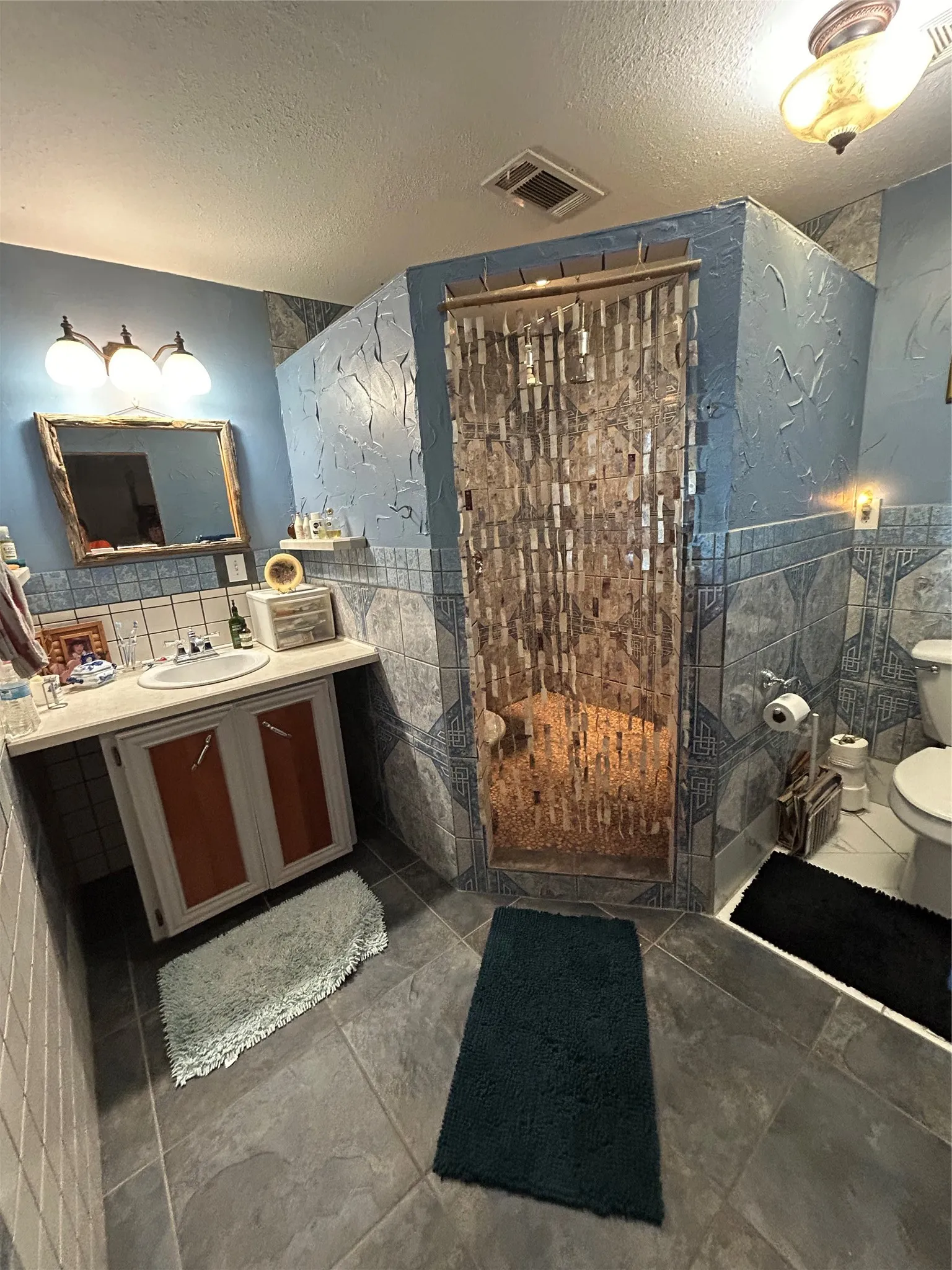 Ceramic tile flooring, built-in vanity with integrated sink, toilet, and tiled shower enclosure