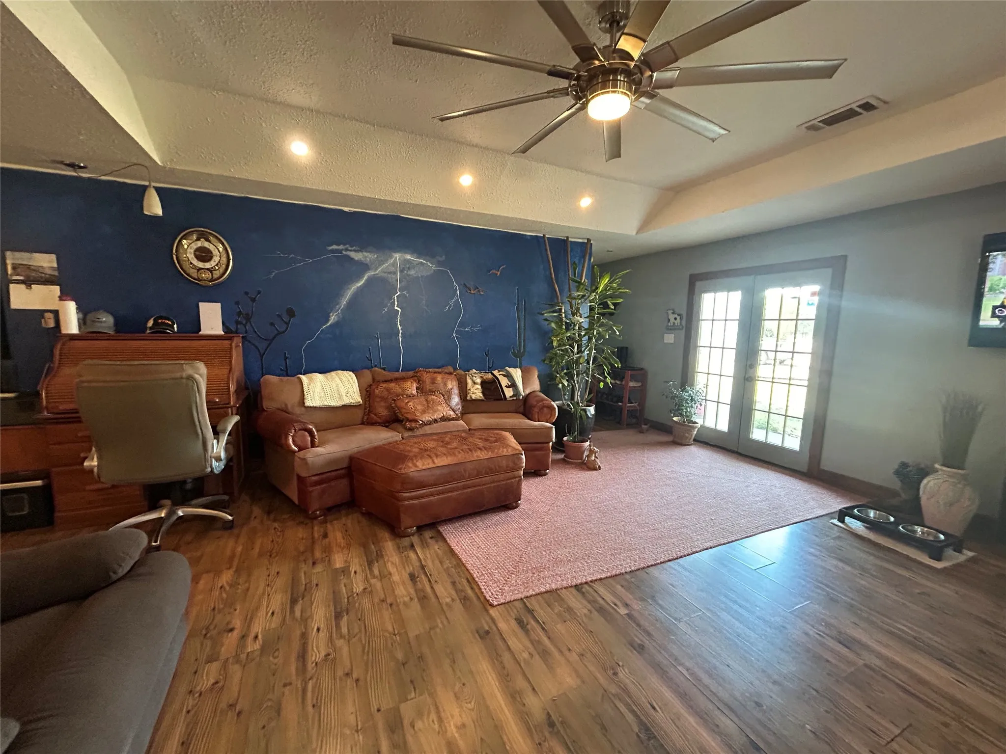 Wood-finish flooring throughout, tray ceiling with a ceiling fan, recessed lighting, and double glass doors