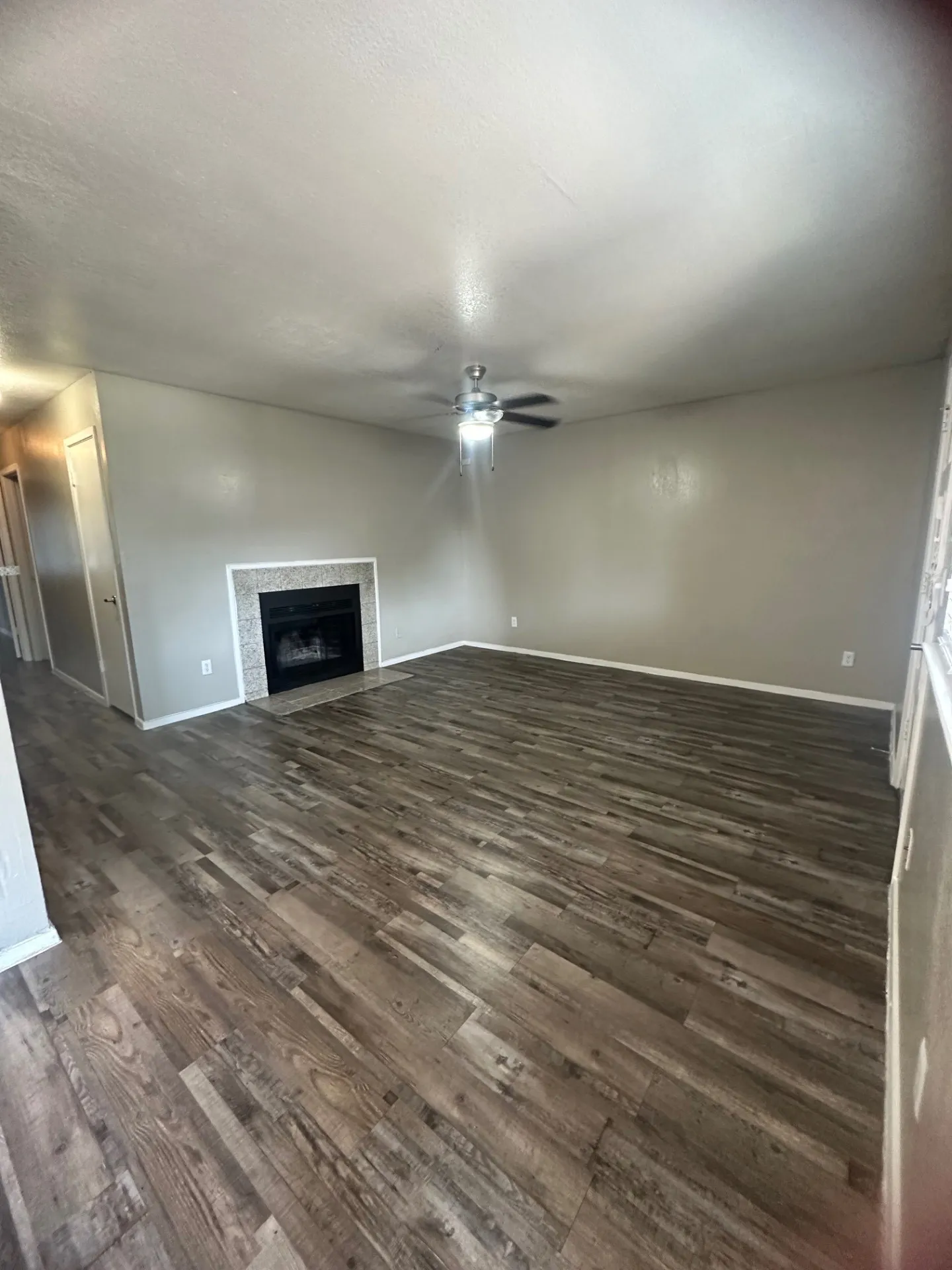 Recessed fireplace with tile surround, wood-finish flooring, ceiling fan with integrated lighting, and neutral wall tones