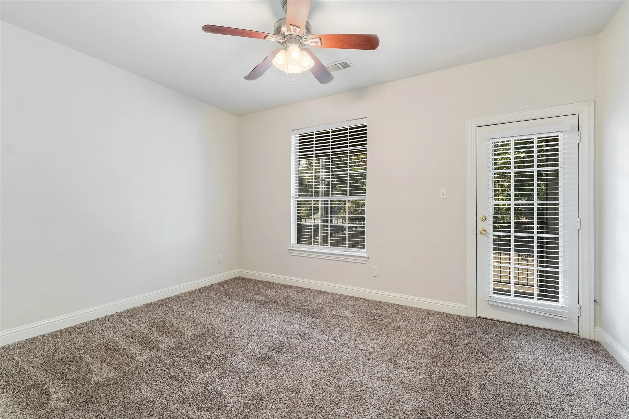 Neutral wall paint, textured carpeting, ceiling fan with light fixture, window with blinds, and a glass-paneled door