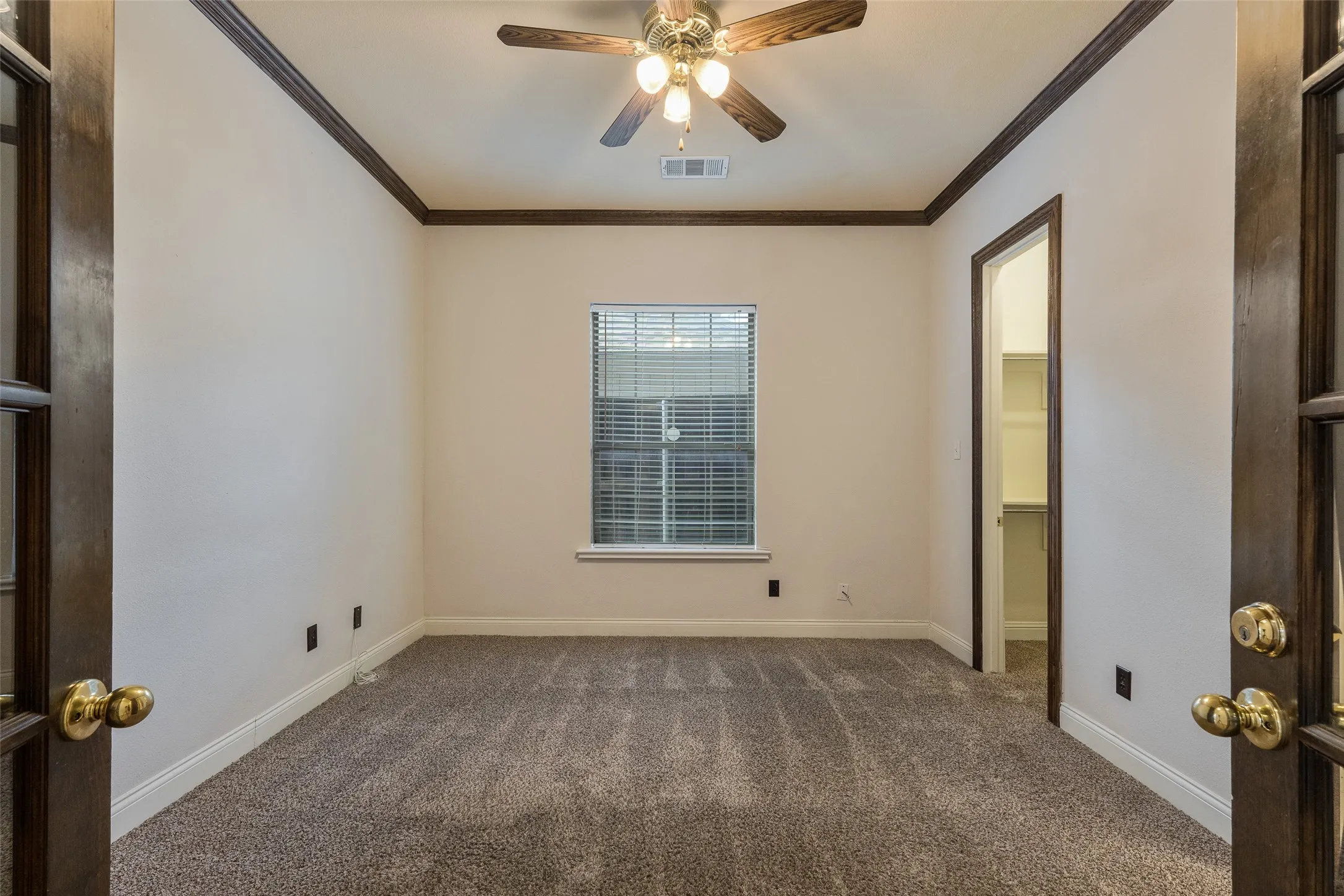 Carpeted room featuring a ceiling fan with light fixture, window with blinds, and built-in closet shelving