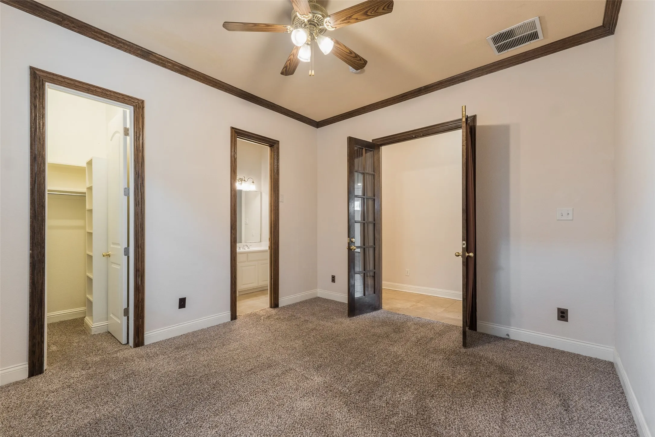 Vaulted ceiling with a ceiling fan, carpeted flooring, dark wood-finish trim, French doors, and built-in closet shelving