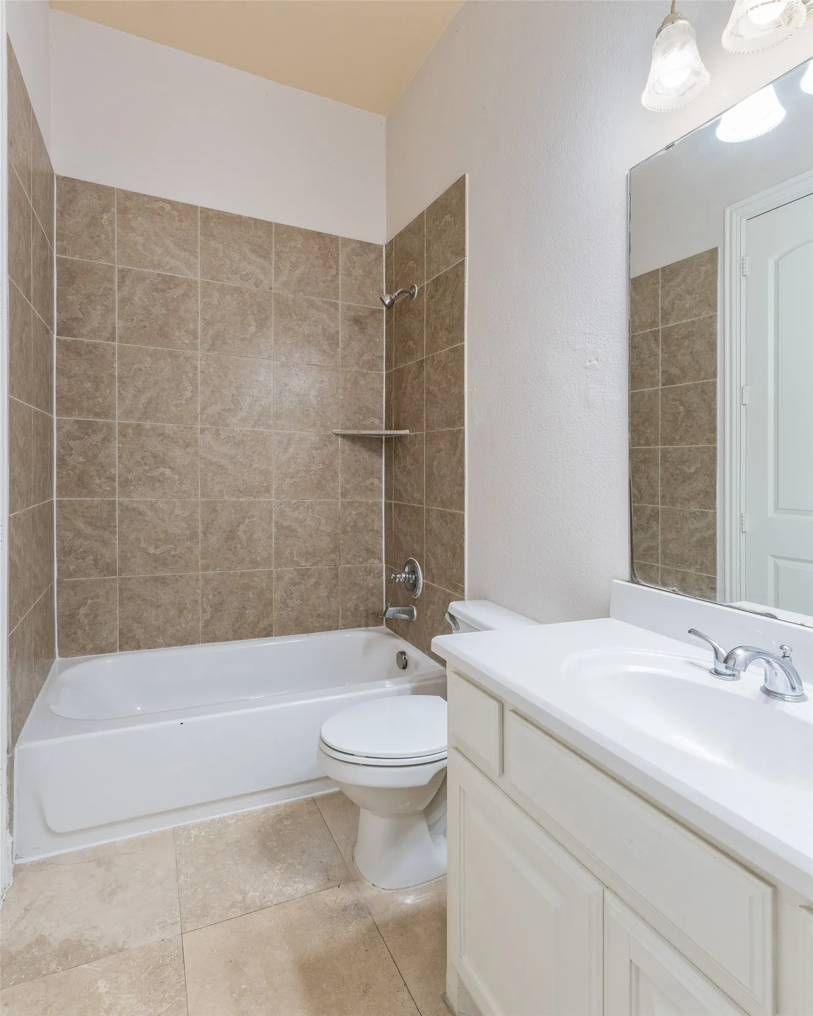 Tile flooring, white vanity with integrated sink, chrome faucet, wall-mounted mirror, and a tiled shower/tub combination