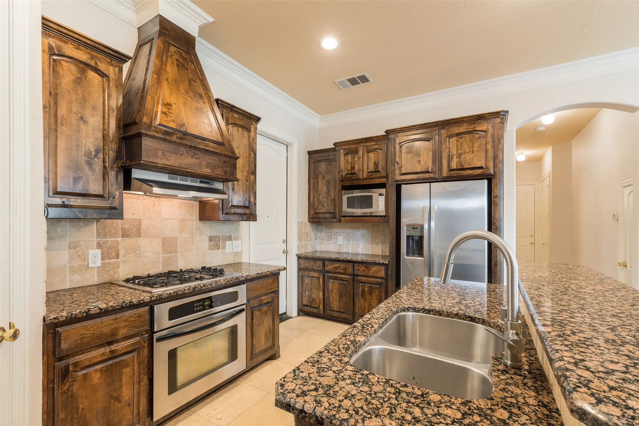 Kitchen featuring wood cabinetry, granite countertops, stainless steel appliances, a gas range with an oven, and a double basin sink with a high-arc faucet
