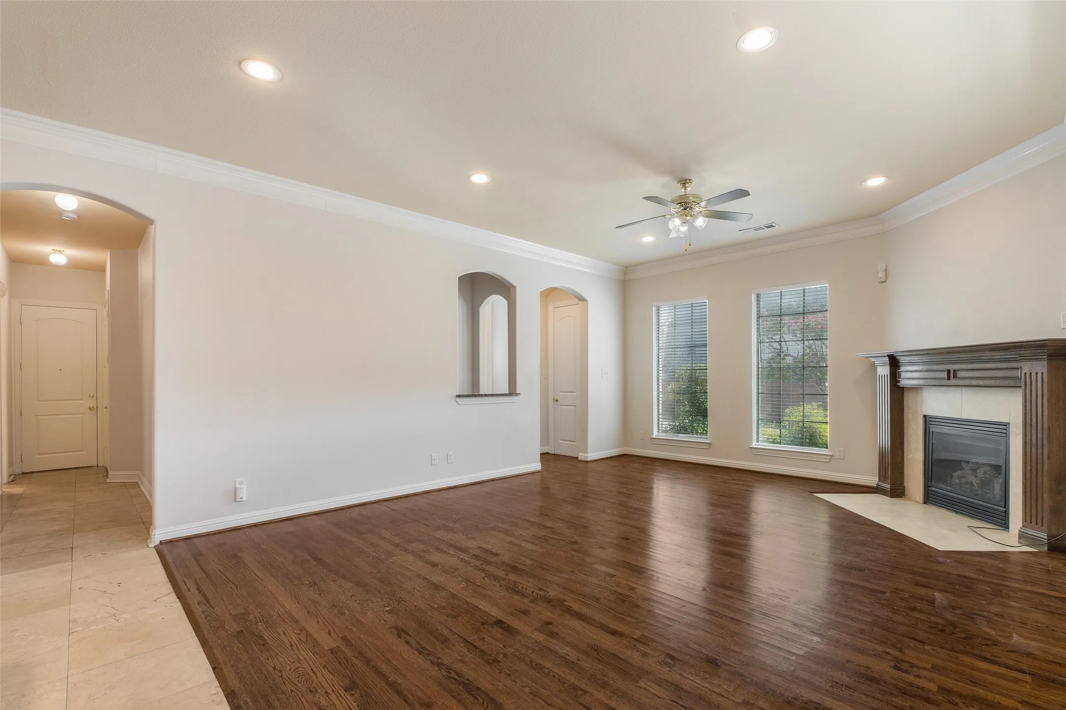 Spacious living area featuring wood-finish flooring, a decorative fireplace with mantel, recessed lighting, and crown molding