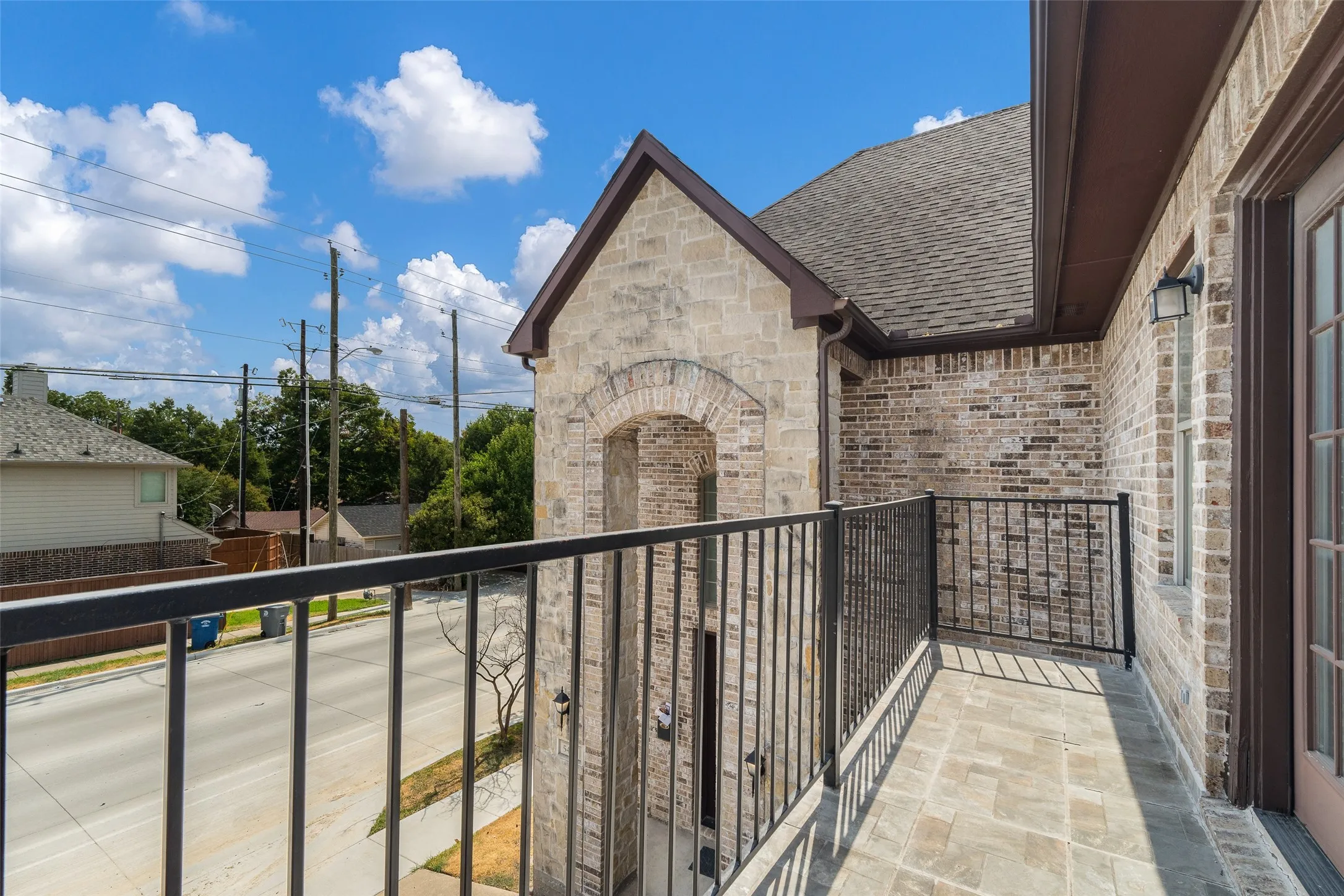 Balcony with tile flooring, wrought iron railing, brick exterior, stone accent wall, and a full-light door