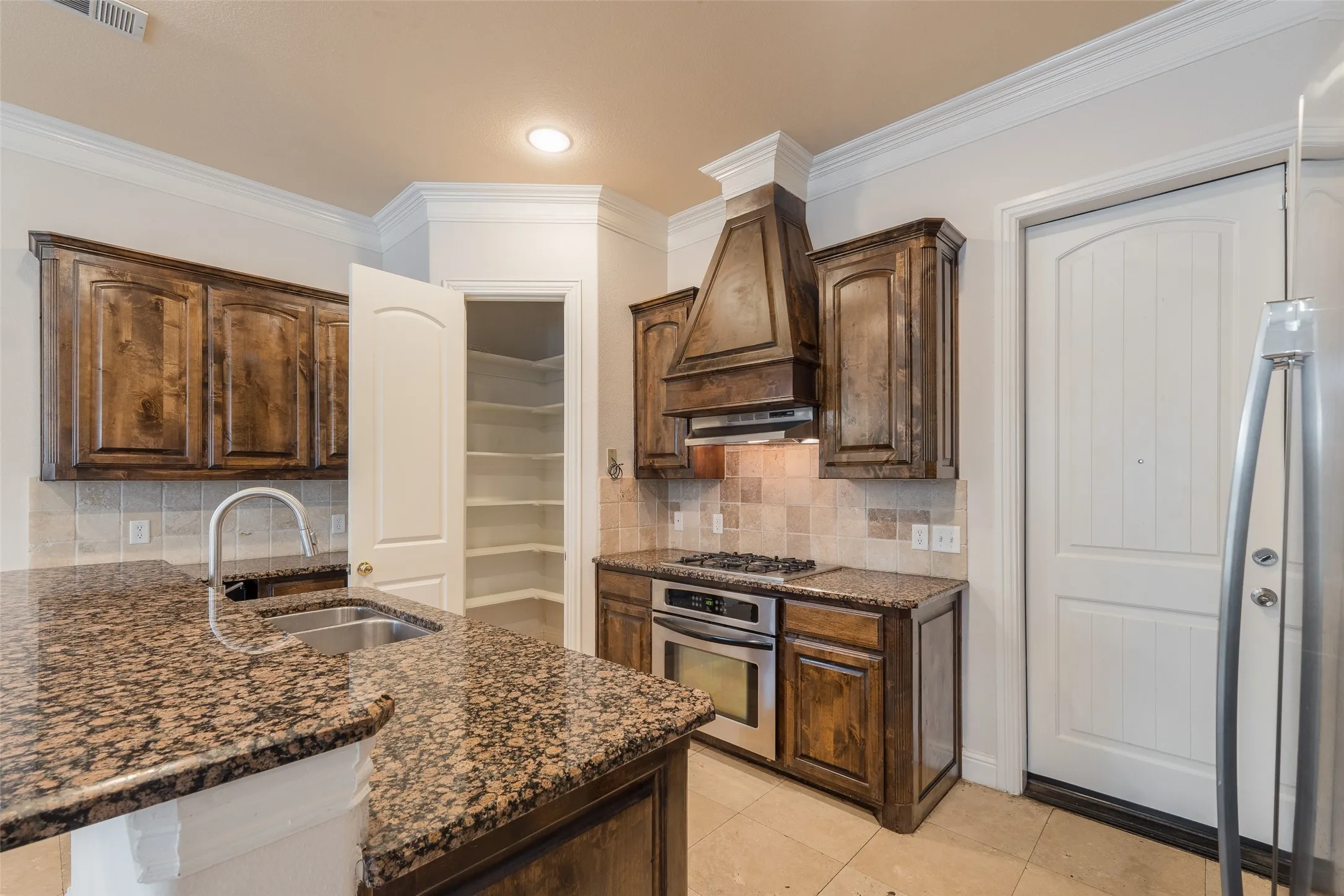 Kitchen featuring granite countertops, wood cabinetry, stainless steel appliances, a tile backsplash, and a built-in pantry