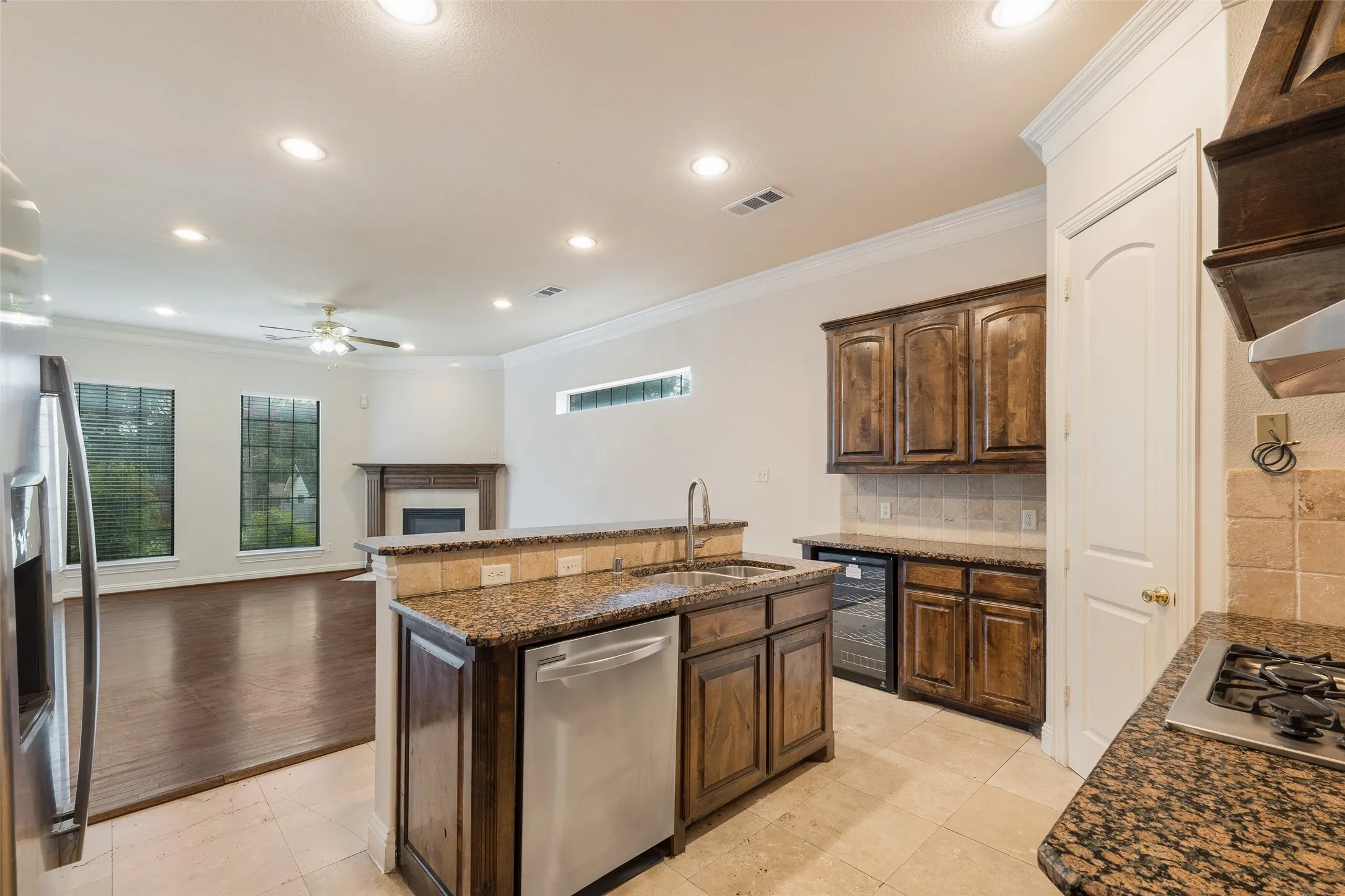 Kitchen island with sink and integrated dishwasher, granite countertops, wood-finish cabinetry, tile flooring, and recessed lighting