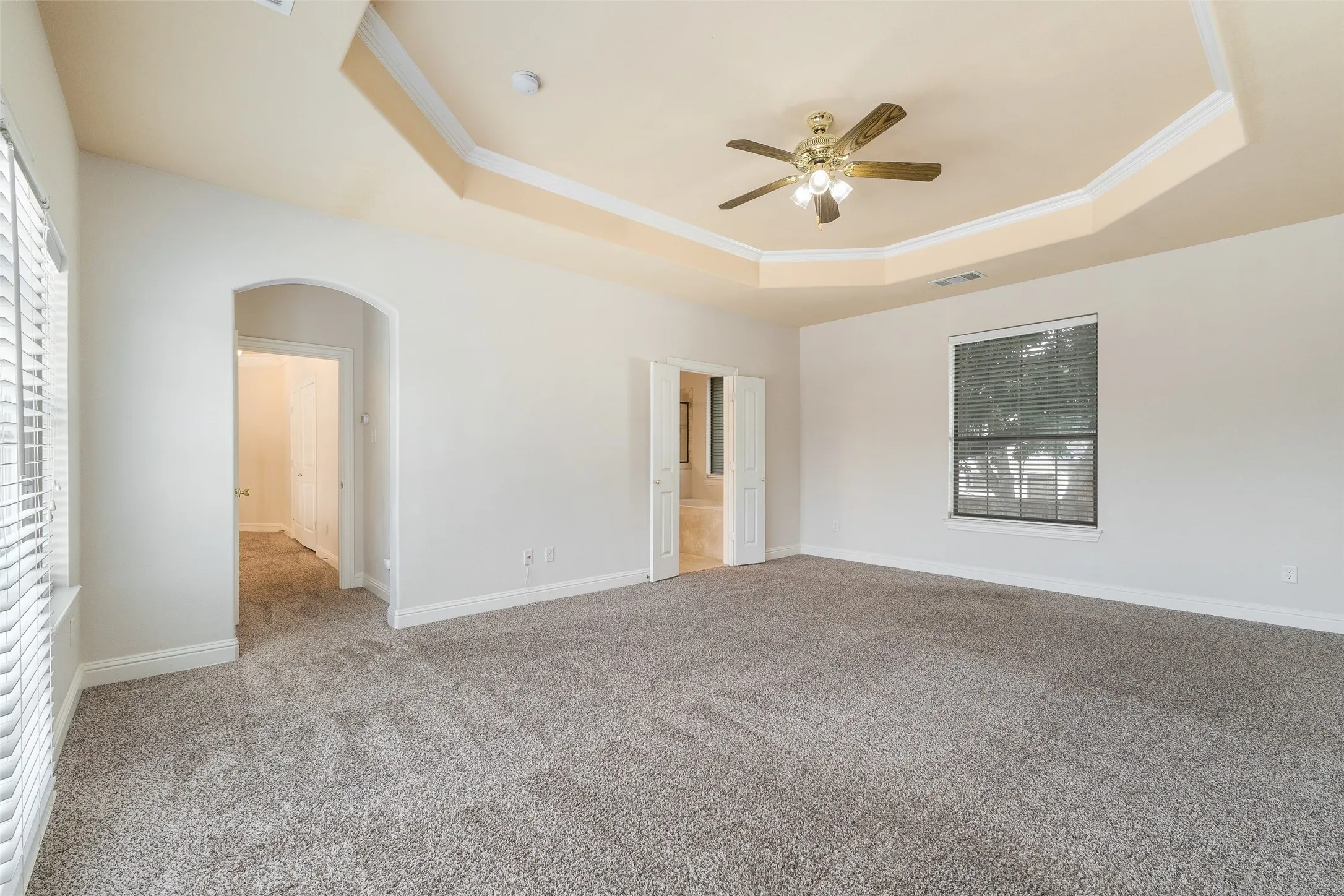 Tray ceiling with crown molding, ceiling fan, and carpeted flooring
