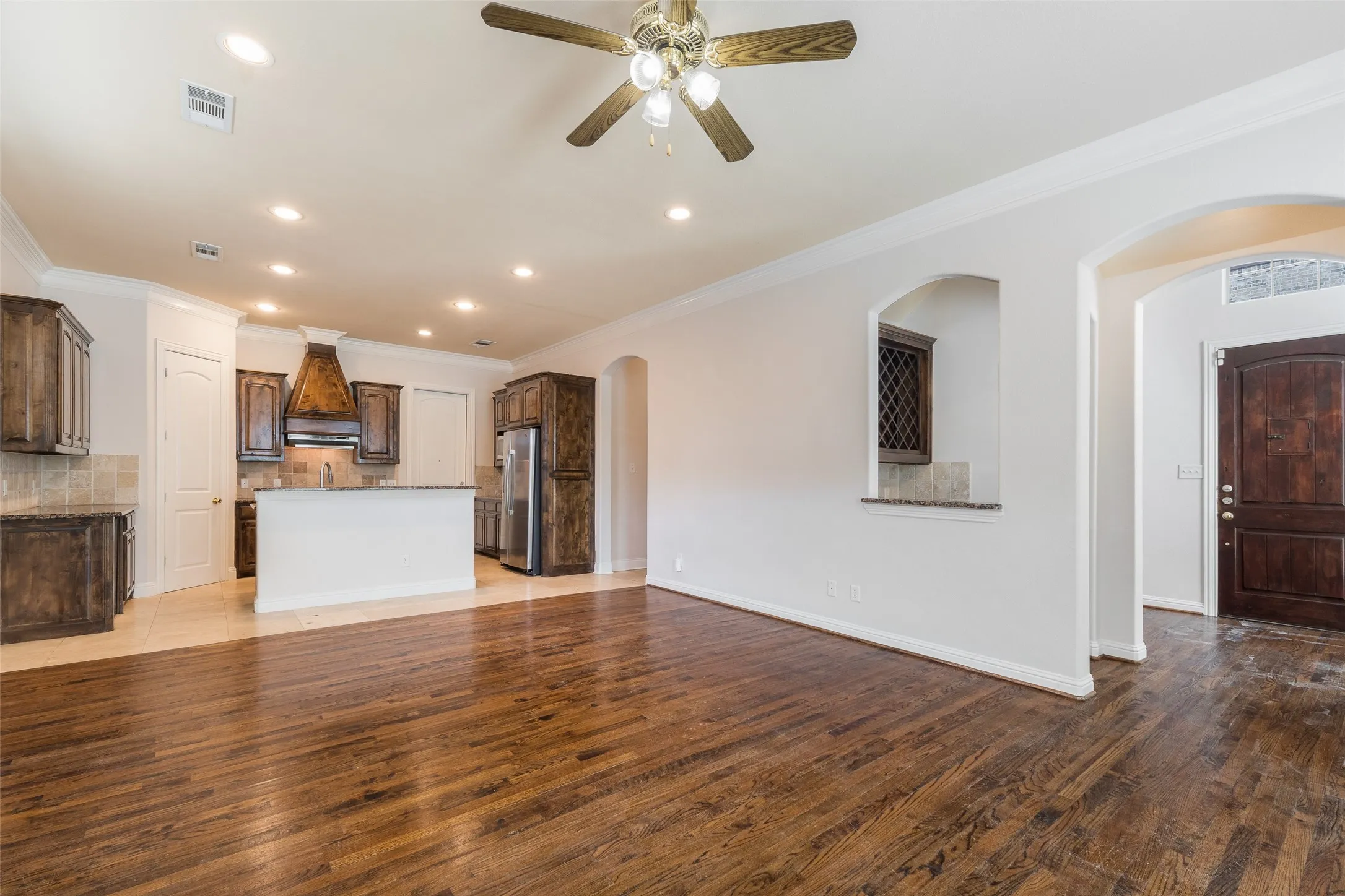 Wood-finish flooring, recessed lighting, crown molding, arched entryways, and a ceiling fan