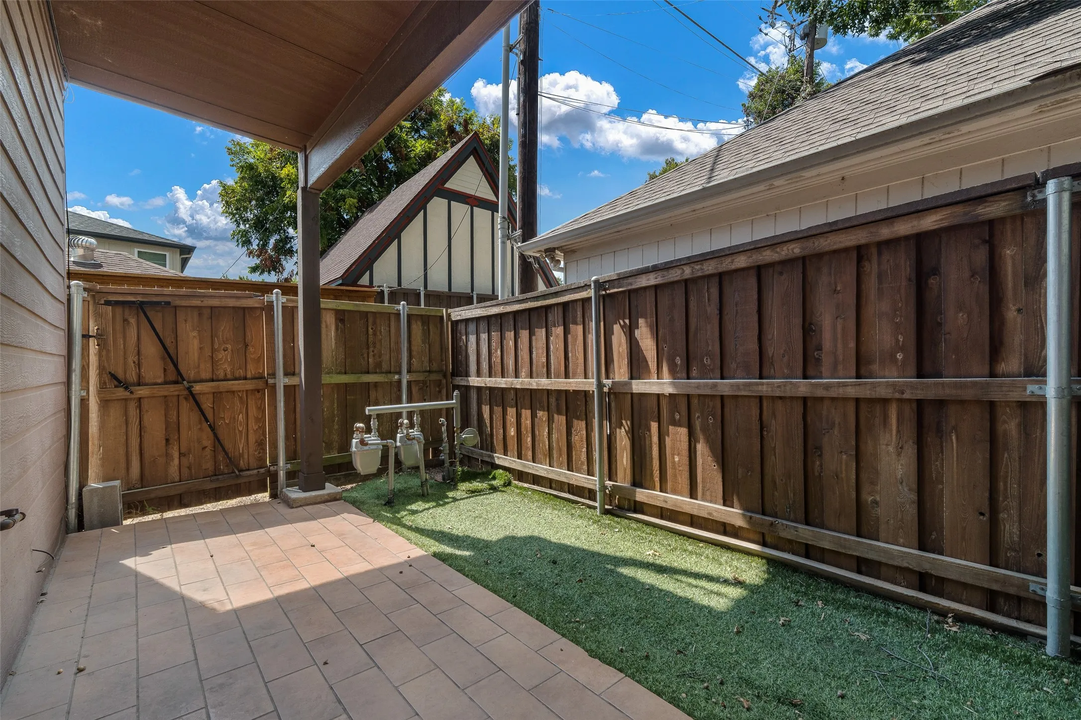 Covered patio with paver flooring and an artificial turf area, enclosed by a wood fence