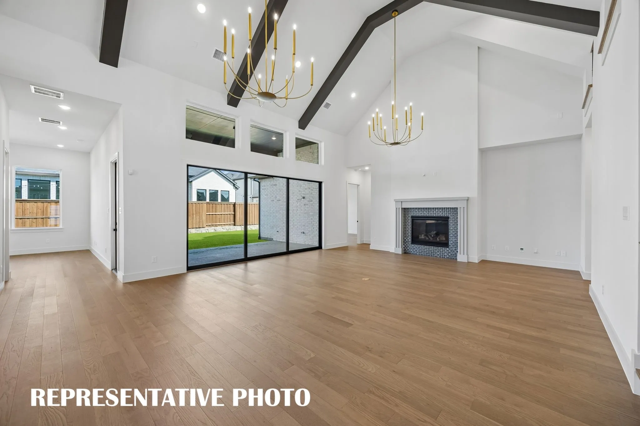 Featuring a full wall slider, beautiful flooring, awe inspiring ceiling beams and grand chandeliers, this great room is an entertainer's dream home come to life!  REPRESENTATIVE PHOTO