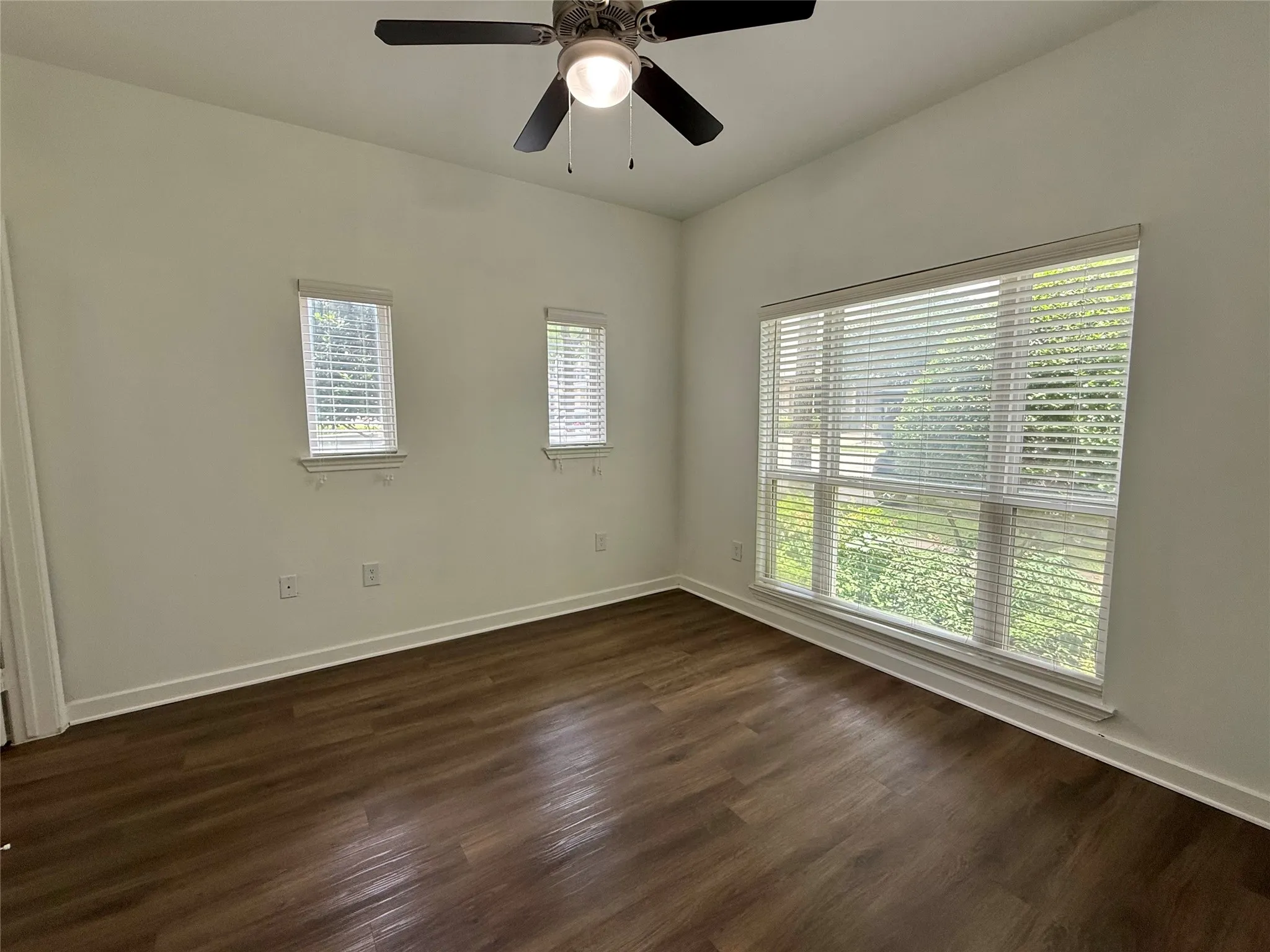 Empty room featuring dark wood finished floors, baseboards, and ceiling fan