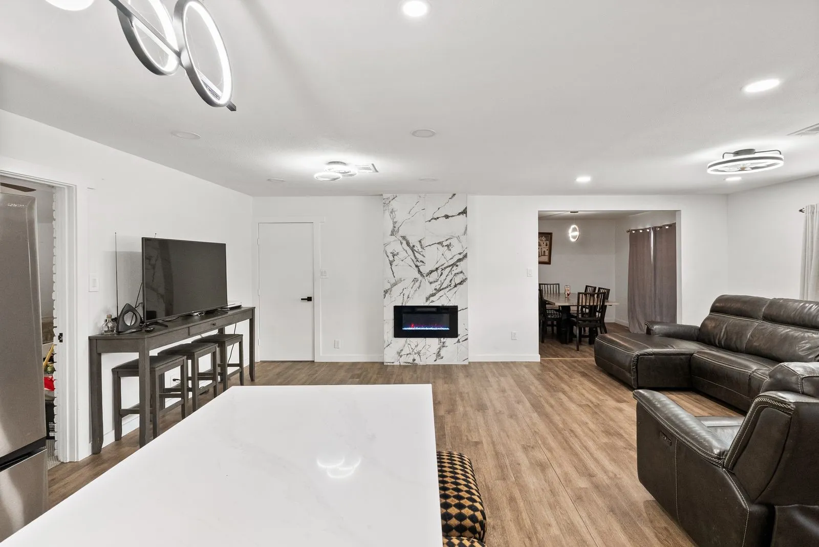 Wood-finish flooring throughout, modern electric fireplace with a floor-to-ceiling stone-look surround, recessed lighting, and contemporary ceiling fixtures