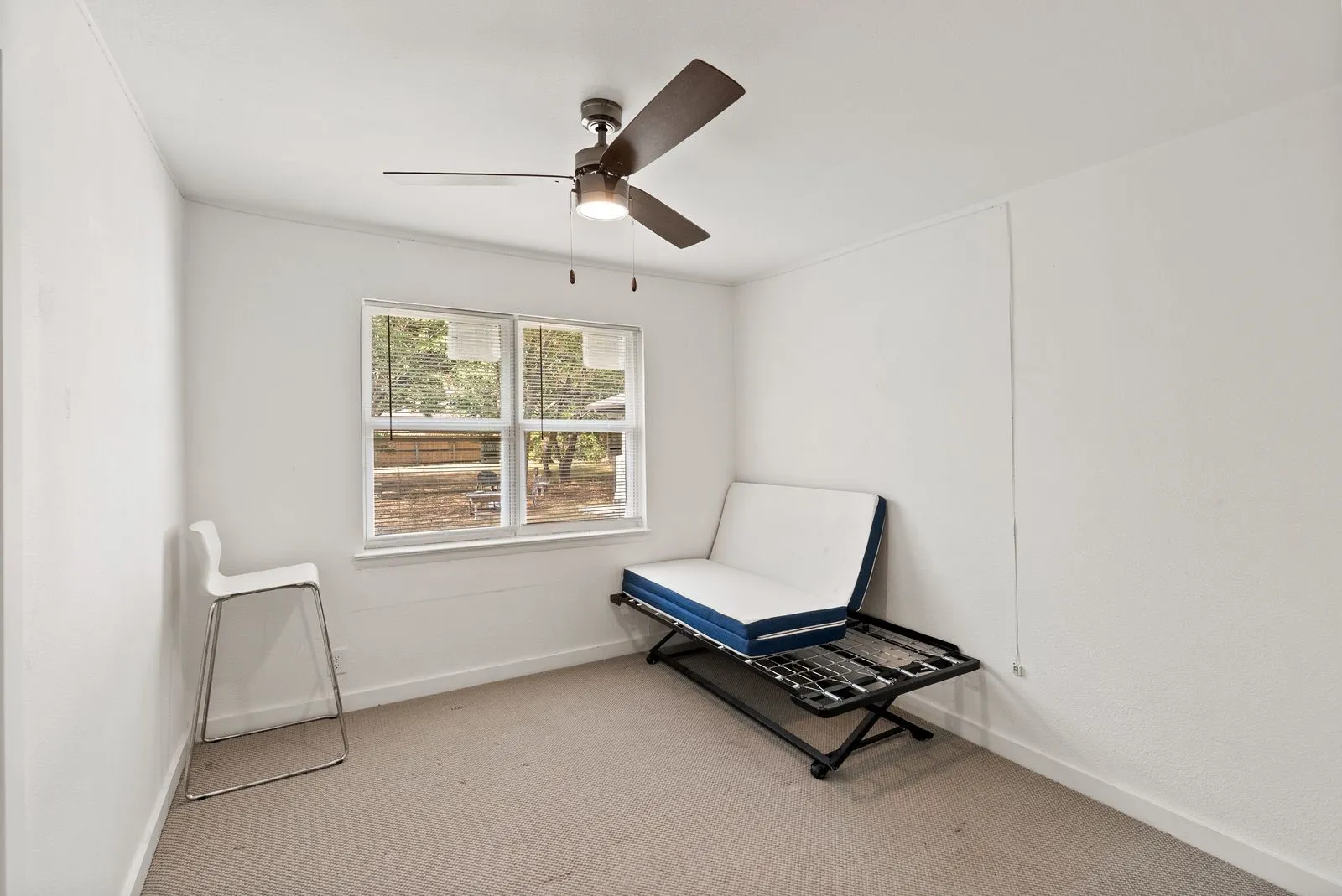 Neutral wall paint, ceiling fan with integrated lighting, window with exterior landscaping, and carpeted flooring