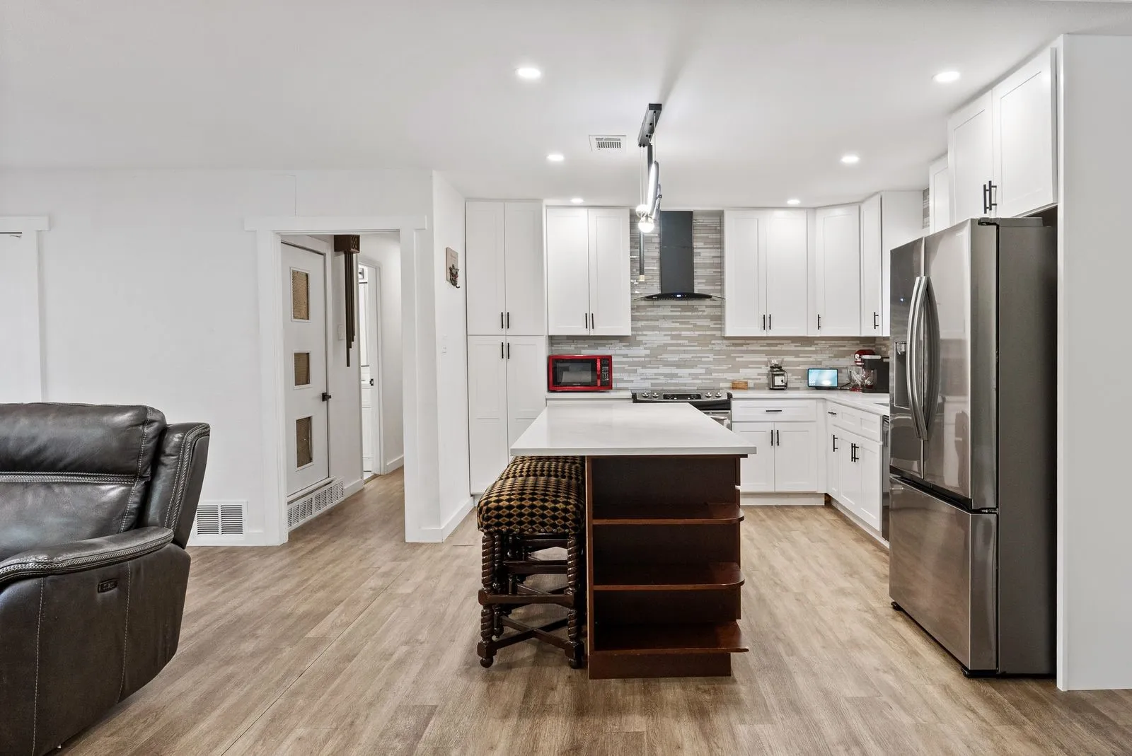 Kitchen featuring white cabinetry, a central island with integrated shelving, stainless steel appliances, and wood-finish flooring