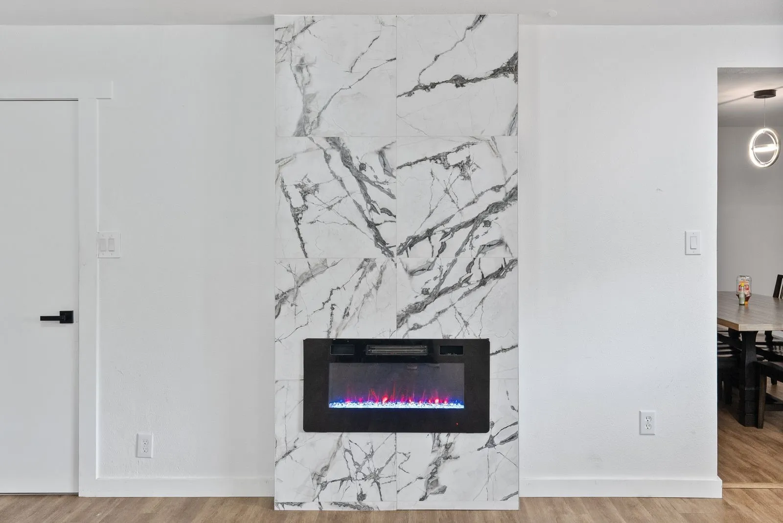 Electric fireplace with a tiled surround, light wood-finish flooring, and white walls