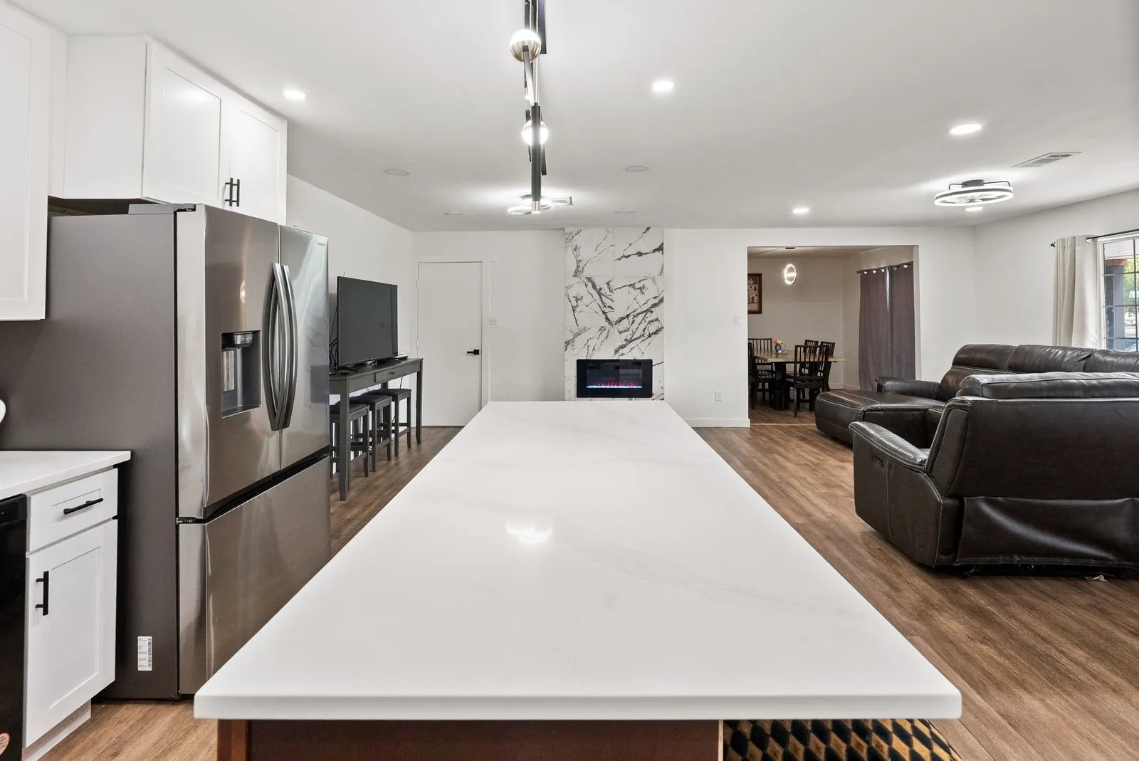 Open-concept living space featuring wood-finish flooring, a contemporary fireplace with a marble-style surround, and recessed lighting