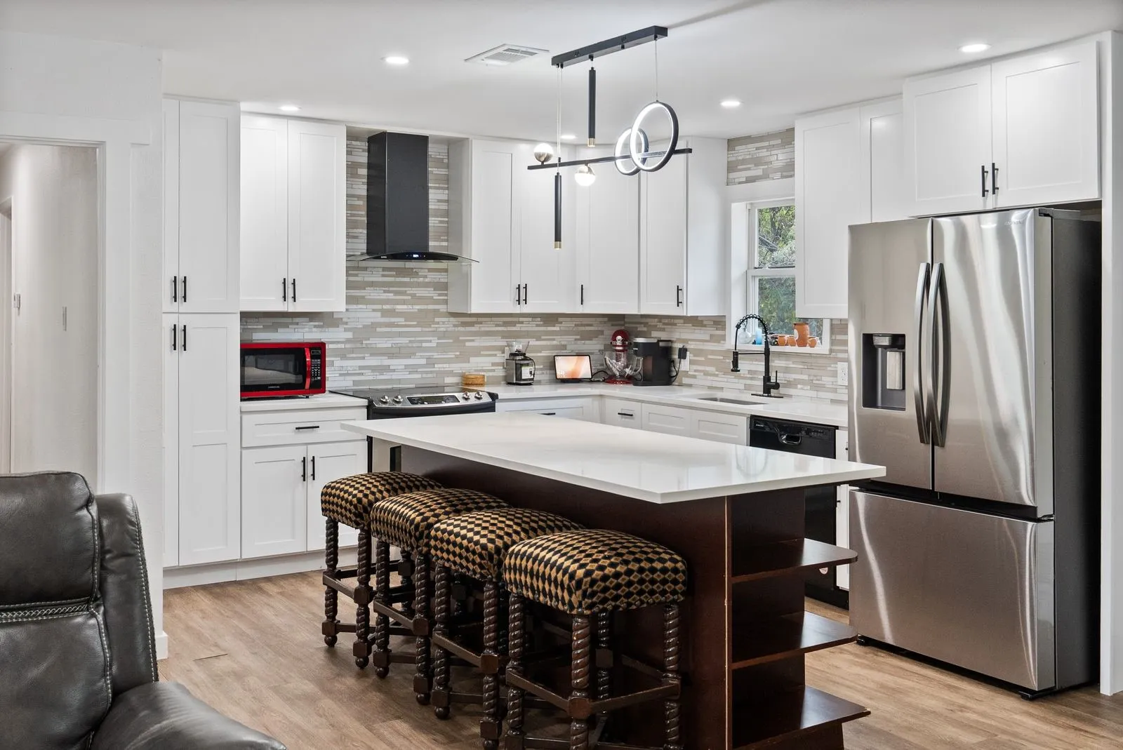 Modern kitchen featuring white shaker cabinetry, stainless steel appliances, a center island with countertop seating, wood-finish flooring, and a decorative tile backsplash