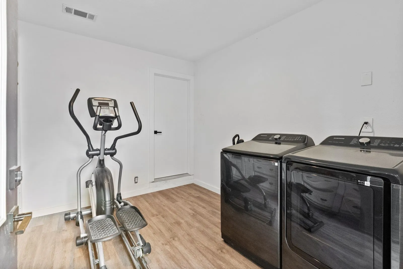 Wood-finish flooring with white walls and a white door featuring a black handle