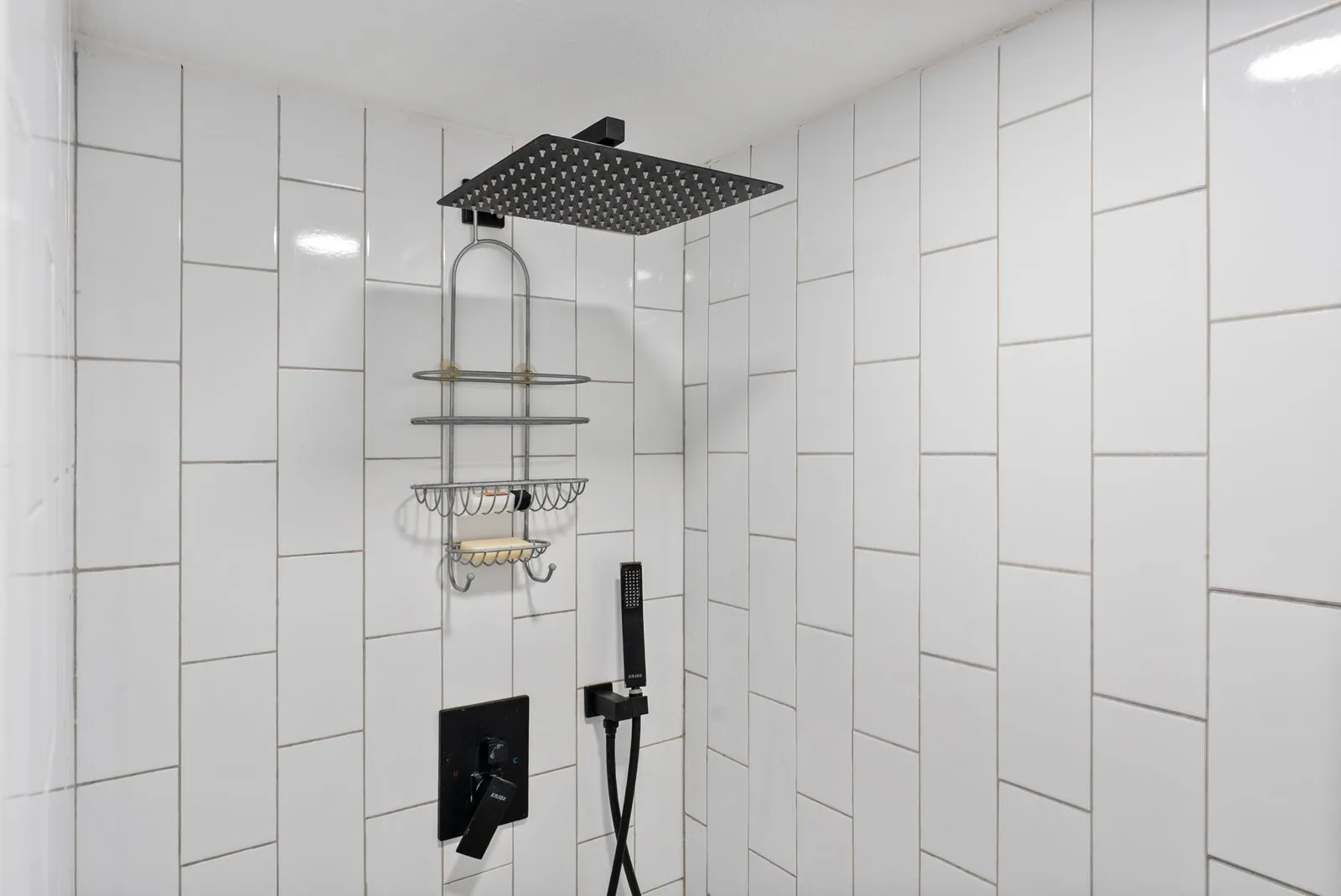 White subway tile surround with a matte black rain shower head, hand-held shower, and control valve