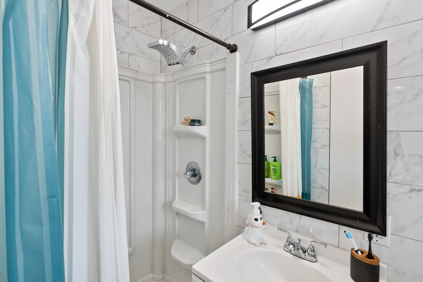White subway tile walls, vanity with integrated sink, chrome faucet, wall-mounted light fixture, and framed mirror