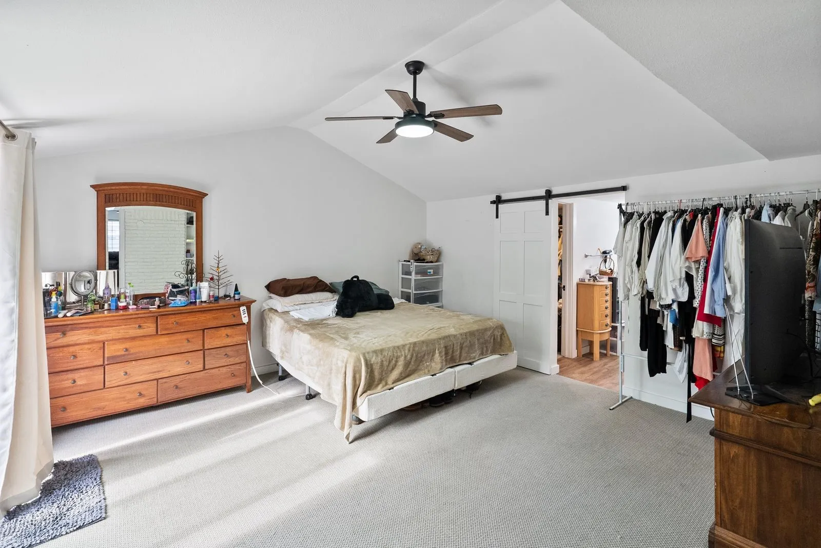Vaulted ceiling, ceiling fan, carpeted flooring, barn door, and a built-in clothing rack