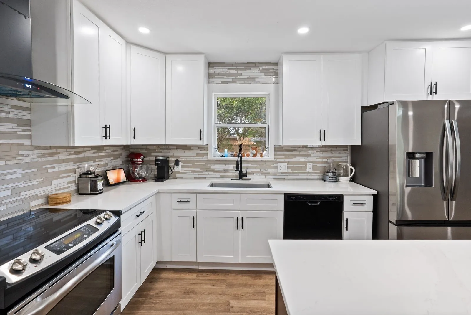 White shaker cabinetry with matte black hardware, mosaic tile backsplash, stainless steel appliances, and a solid surface countertop