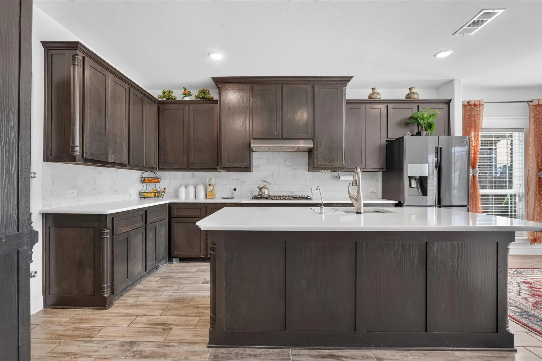 Expansive kitchen featuring dark wood cabinetry, white countertops, a subway tile backsplash, and wood-finish flooring