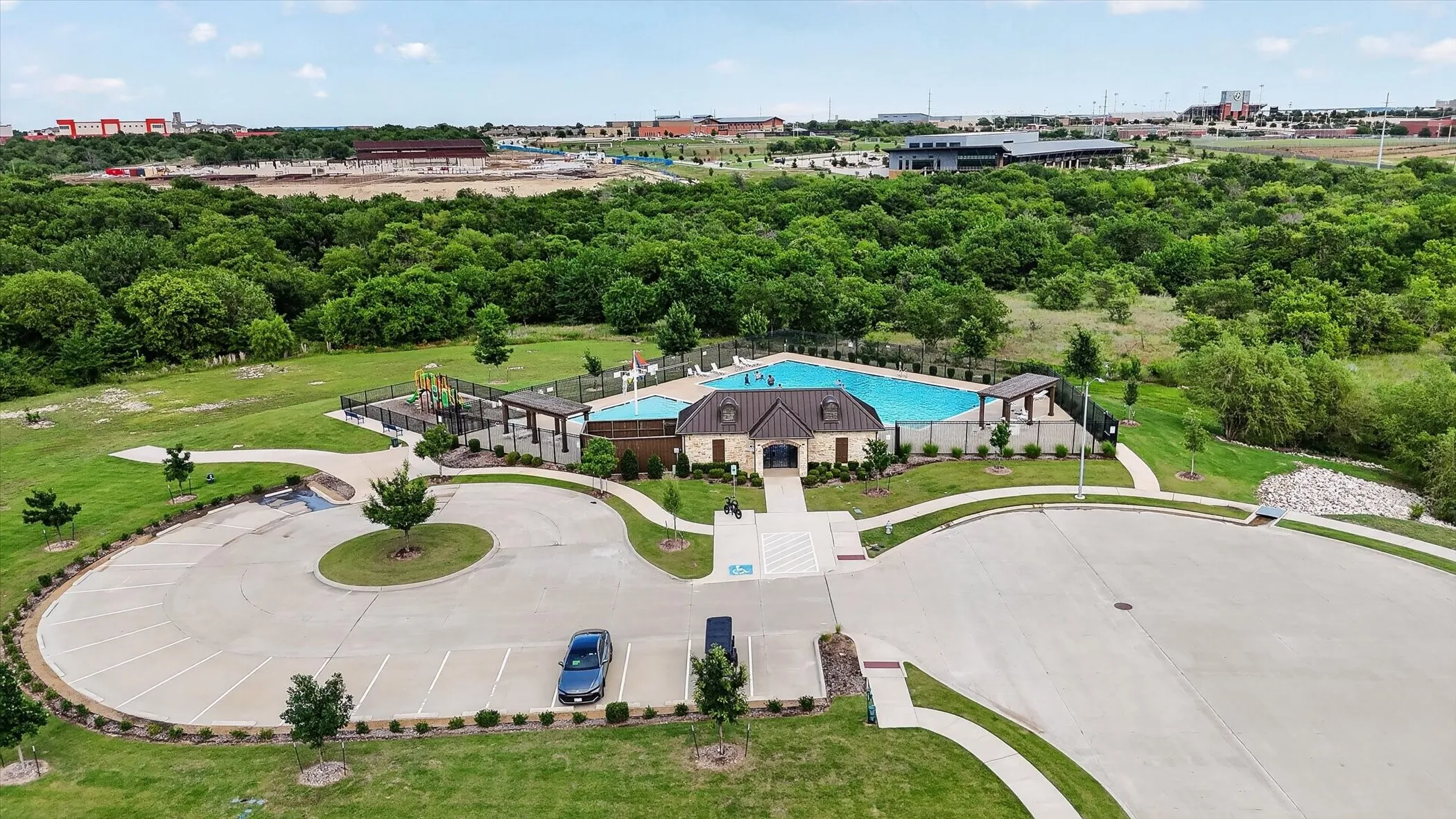Community swimming pool with an adjacent play structure, surrounded by green spaces and mature trees