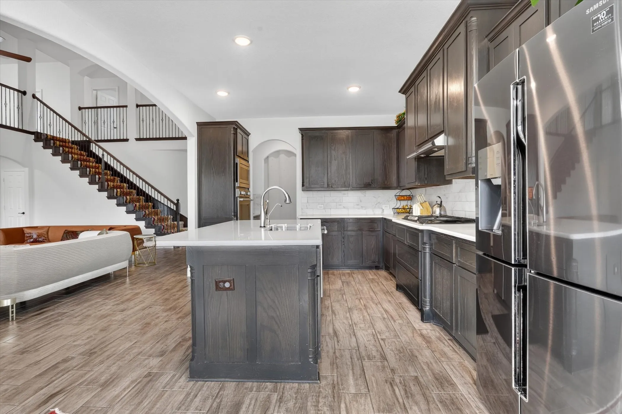 Gourmet kitchen with dark wood-finish cabinetry, stainless steel appliances, a center island with sink, and wood-finish flooring