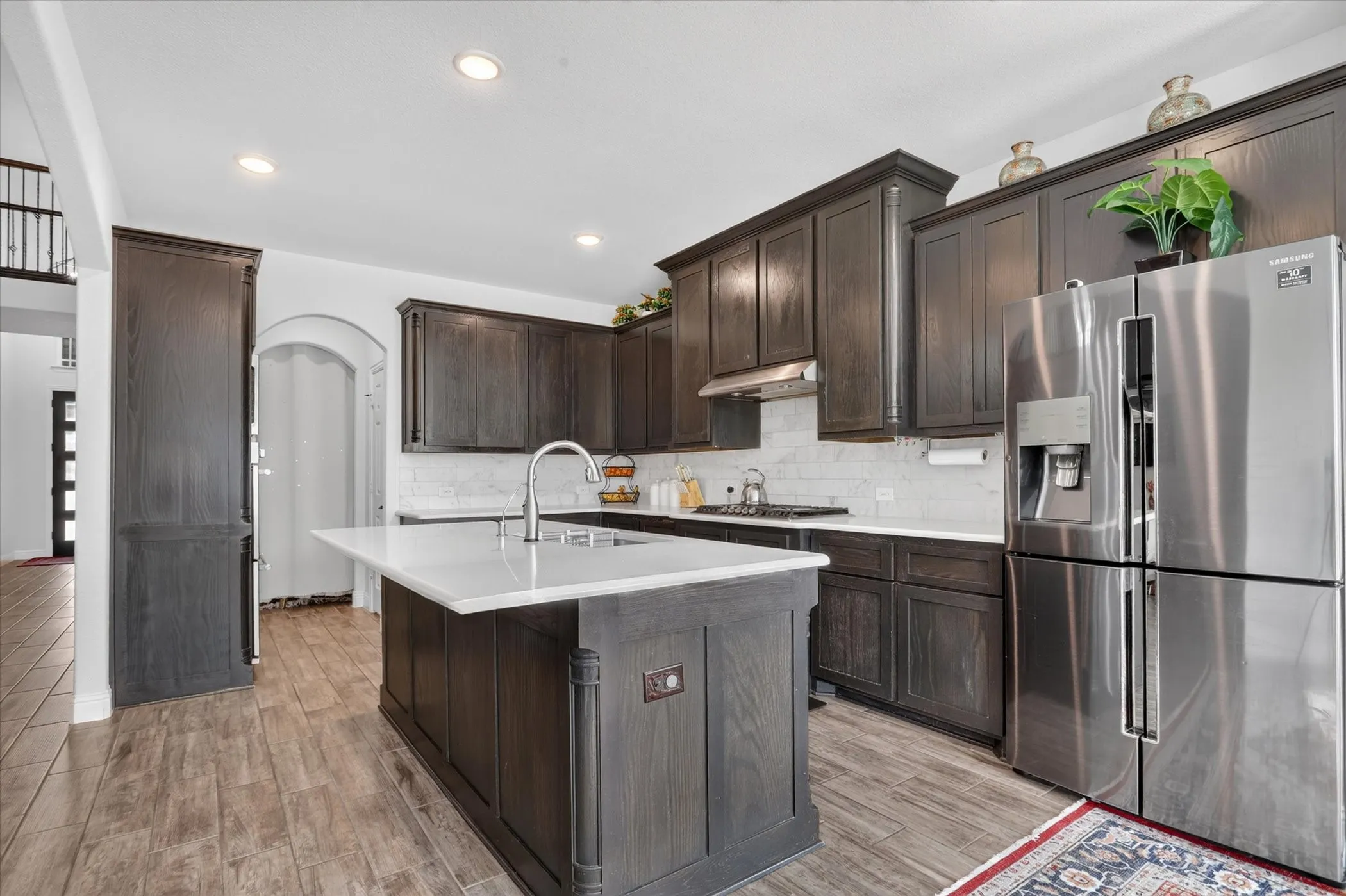 Kitchen featuring dark wood-finish cabinetry, white countertops, white subway tile backsplash, a stainless steel refrigerator, and wood-finish flooring