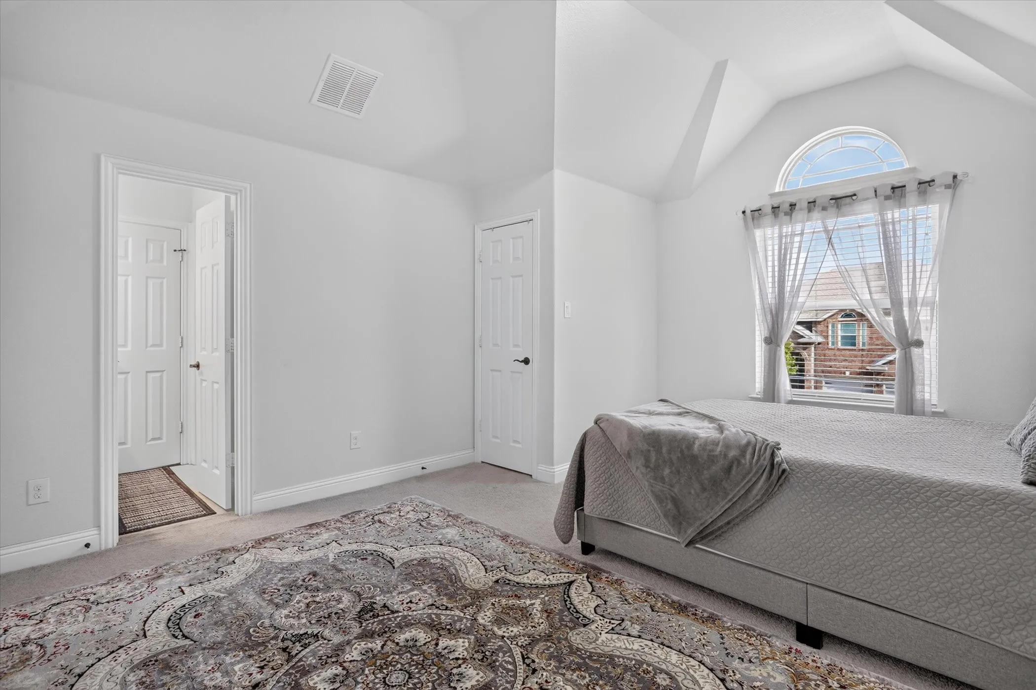 Vaulted ceiling with an arched window, white walls, and wall-to-wall carpeting